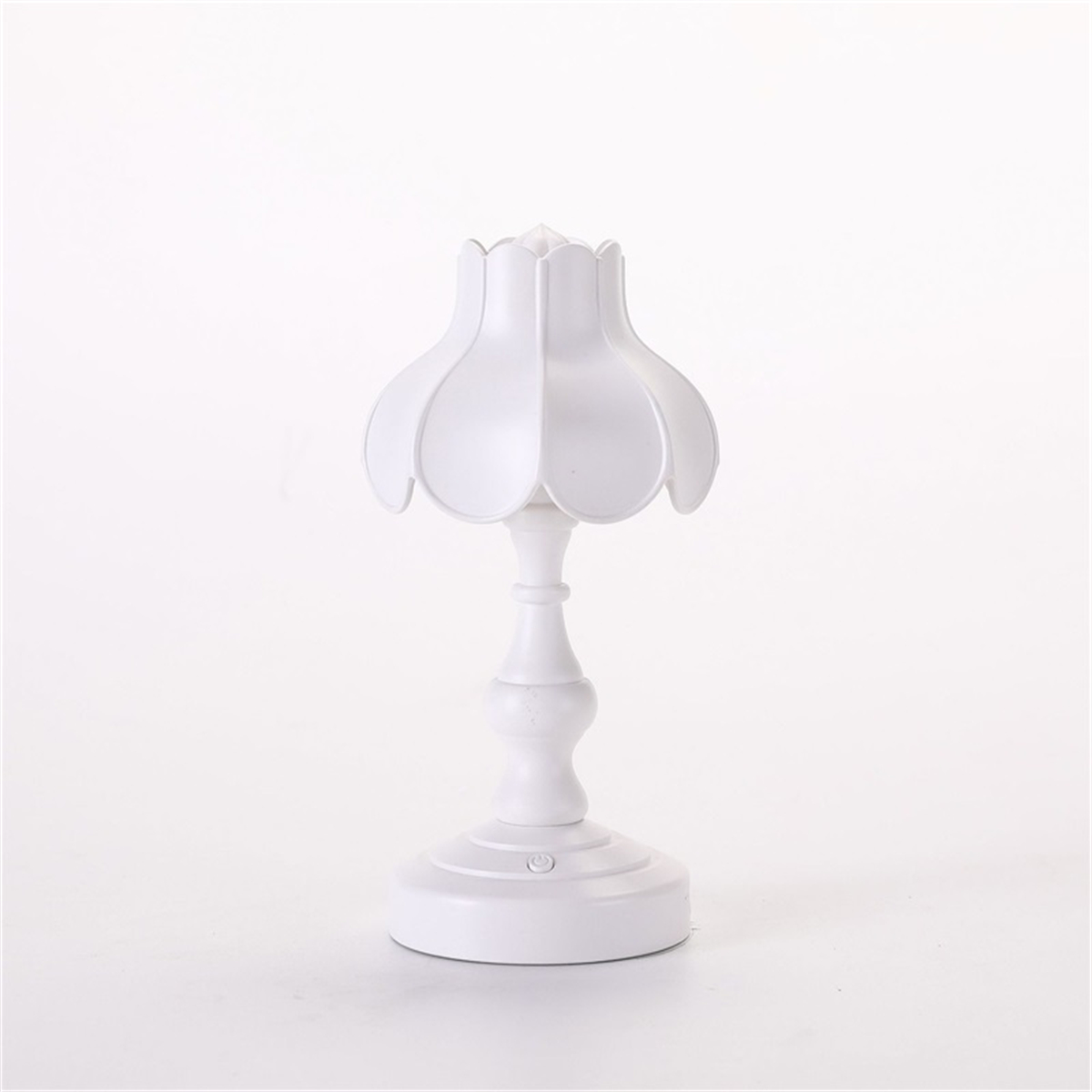 Weiße Tischlampe. Sie hat einen floralen Schirm und einen runden Sockel, auf weißem Grund.