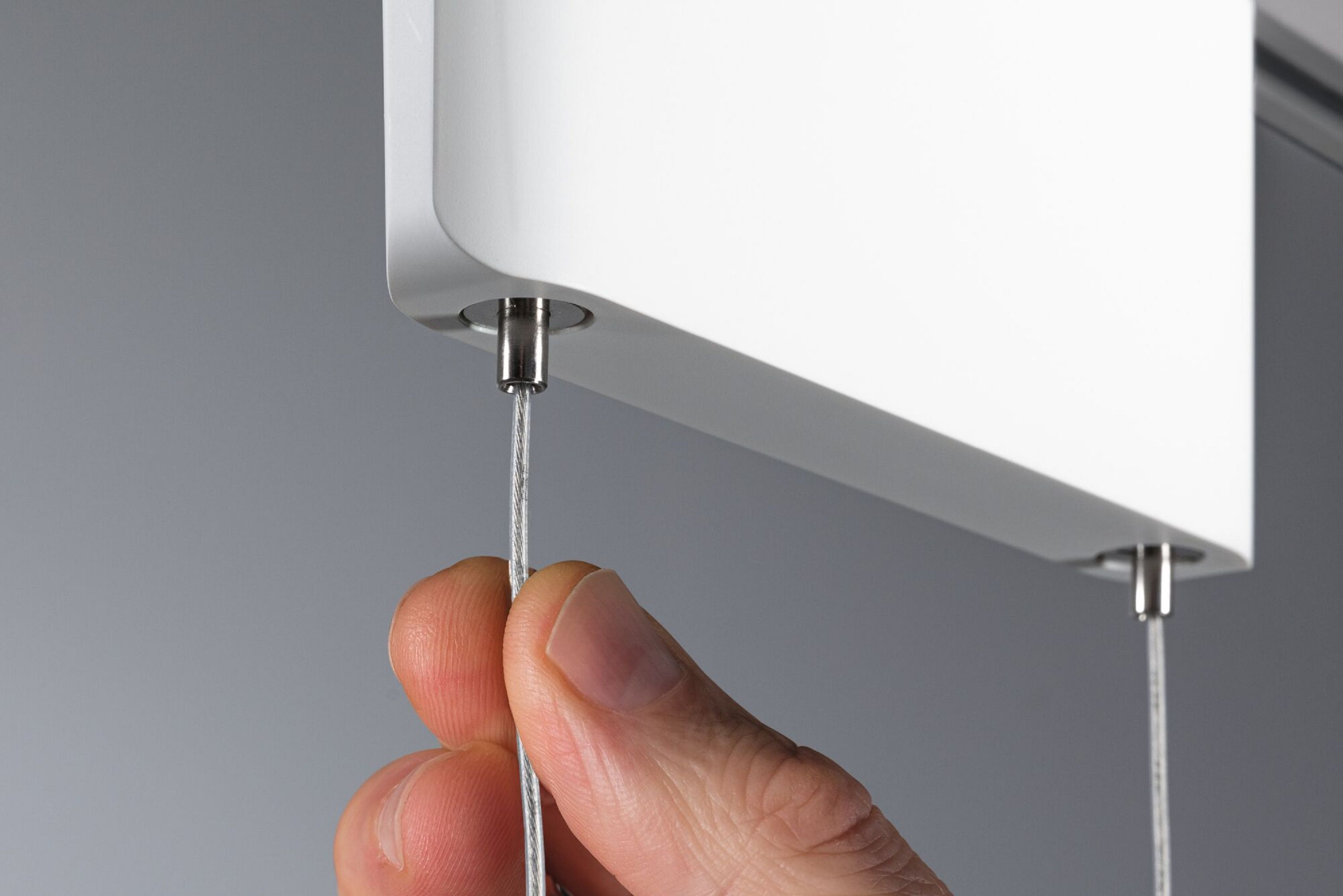 Nahaufnahme einer Hand, die ein Kabel hält, das mit einer weißen Halterung auf grauem Hintergrund verbunden ist.