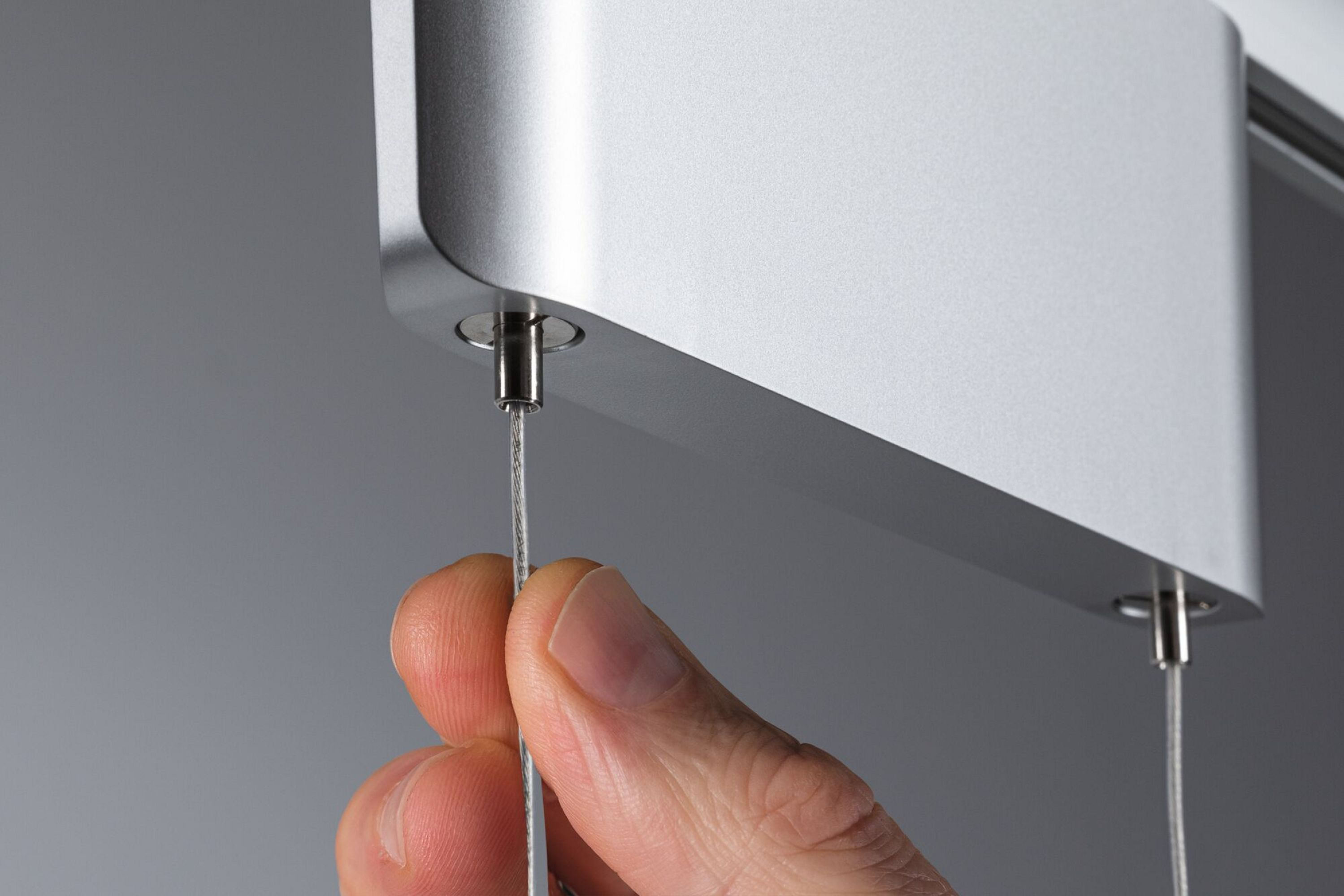 Eine Hand hält einen Draht, der mit einer silbernen Metallstruktur verbunden ist. Der Hintergrund ist grau.