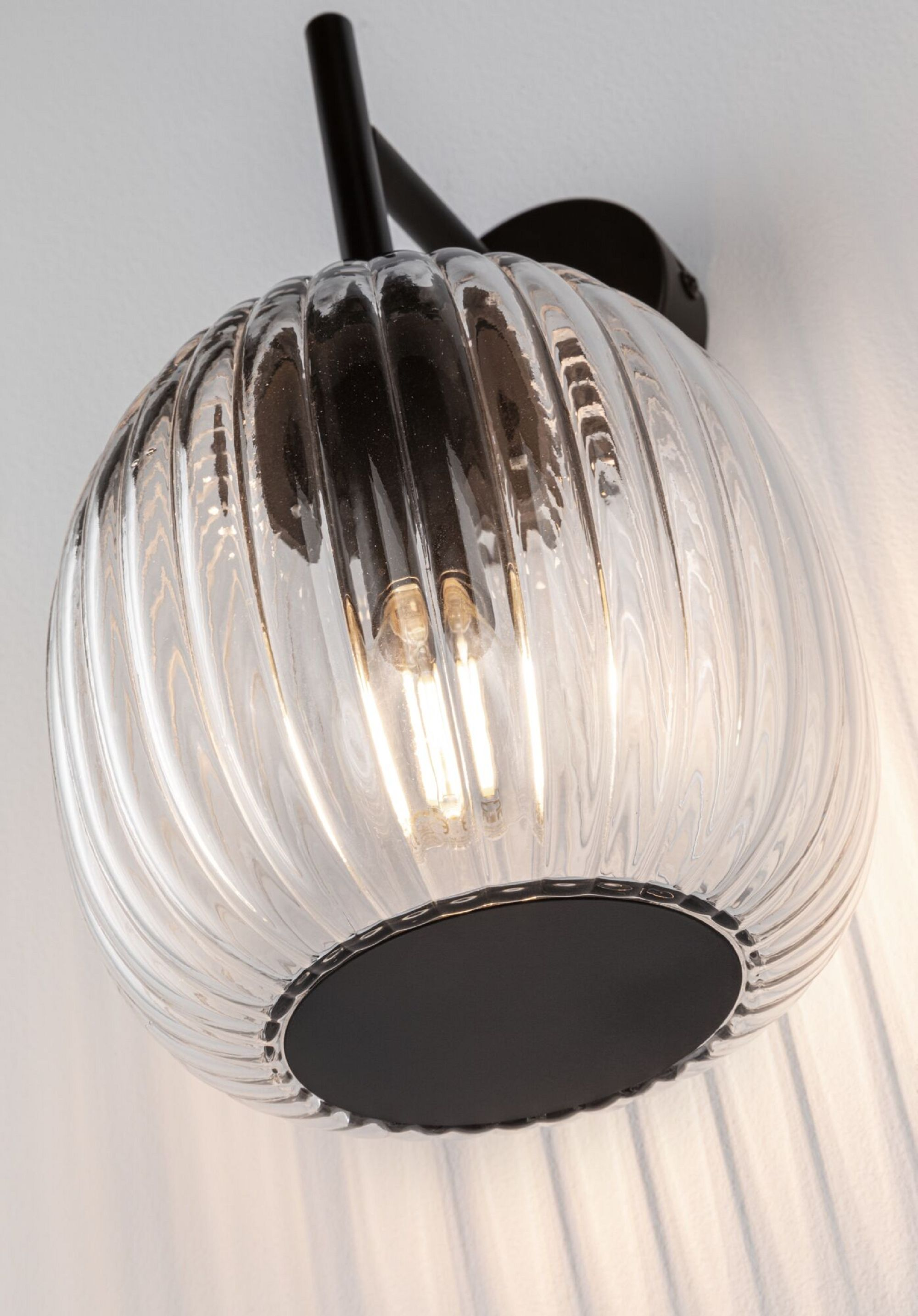 Eine klare Glasleuchte mit schwarzem Metallarm und Sockel, beleuchtet.