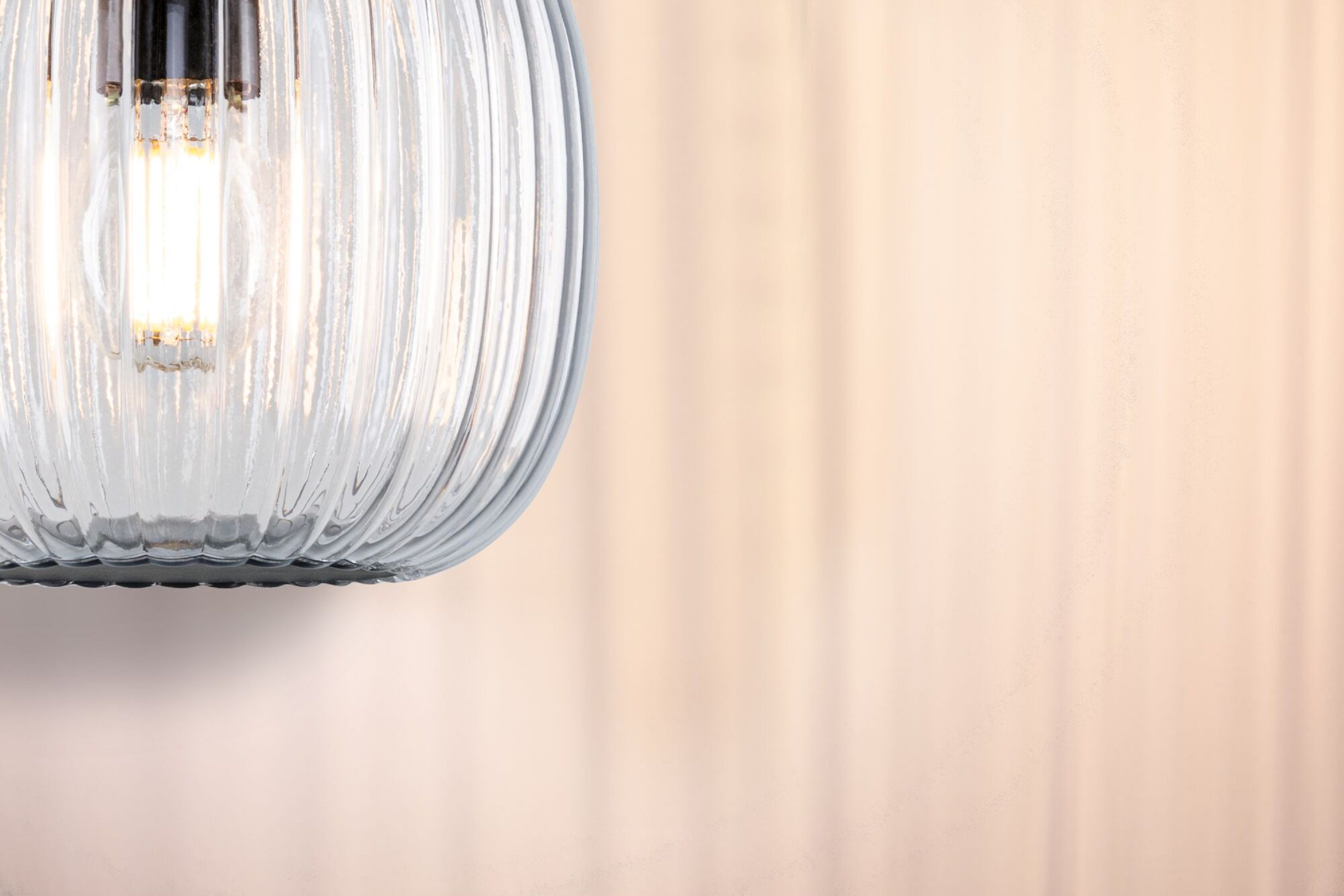 Zbliżenie przezroczystej, żebrowanej szklanej oprawy oświetleniowej z zapaloną żarówką.