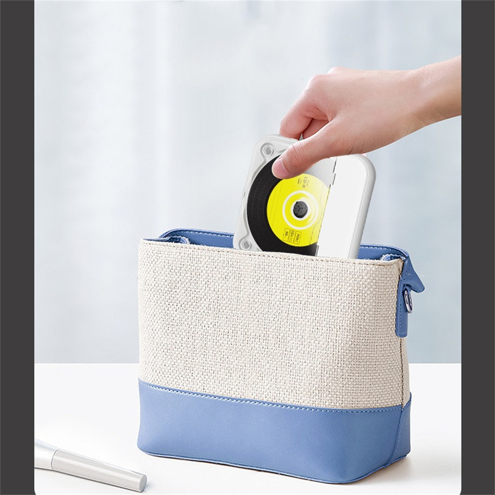 Hand legt eine Disc in eine weiße Hülle in einer blau-beige Tasche, heller Hintergrund.