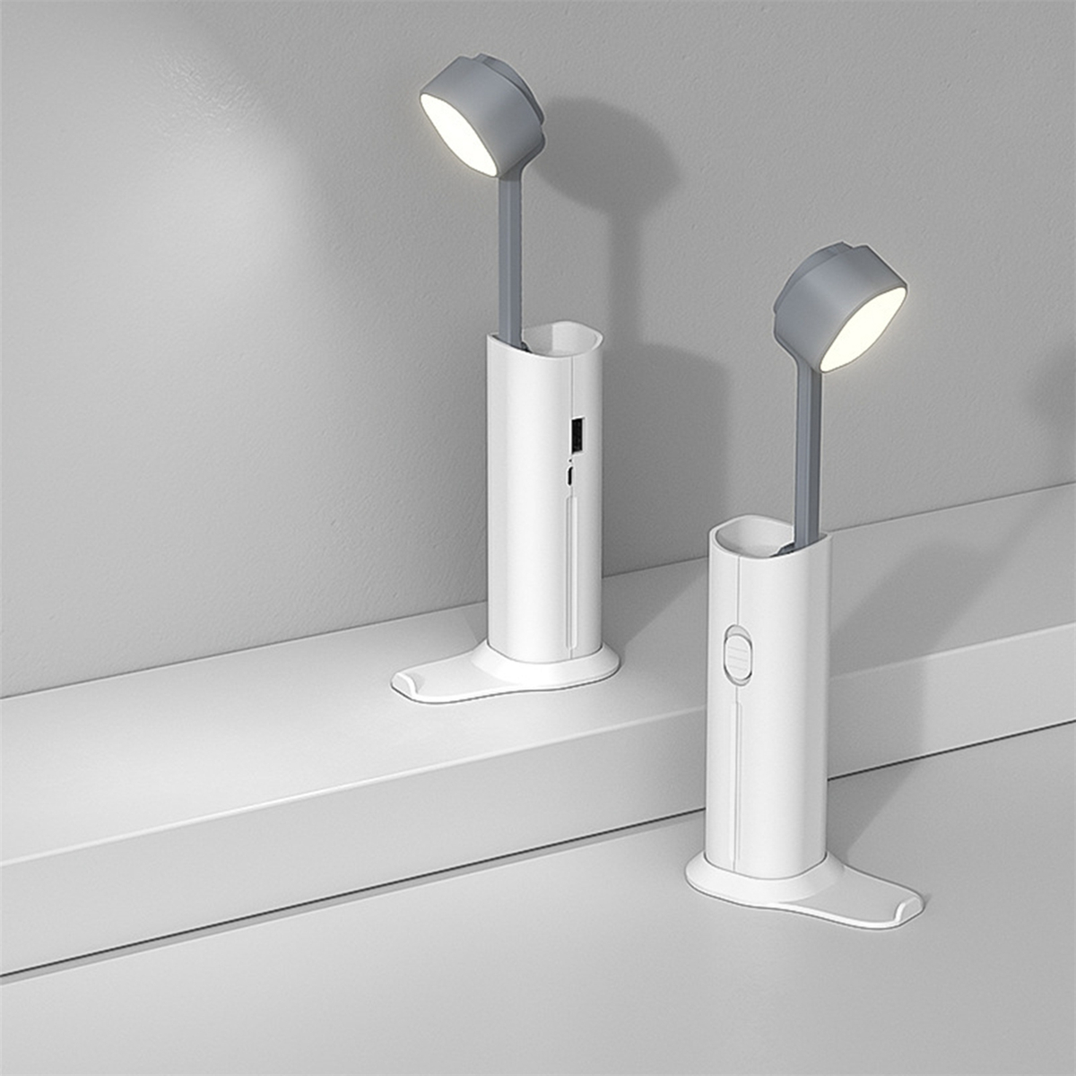 Zwei weiße und graue Schreibtischlampen. Die Lampen stehen auf einer weißen Oberfläche vor grauem Hintergrund.