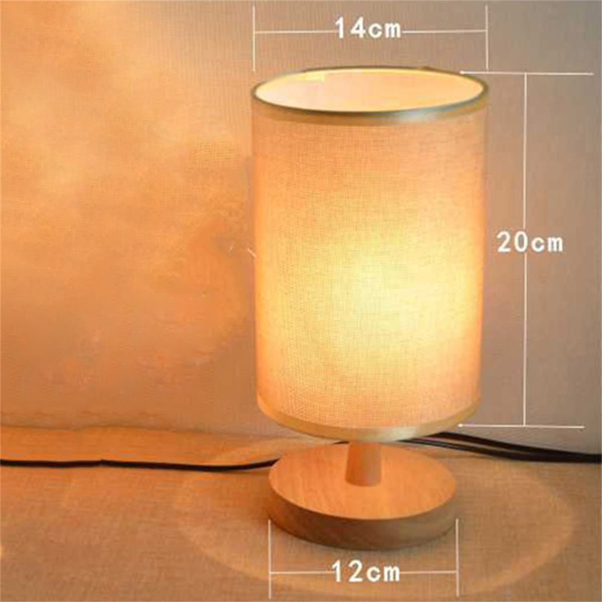 Zylinderförmige Lampe mit beigem Schirm, Holzfuß und beschrifteten Maßen. Hintergrund ist eine cremefarbene Wand.
