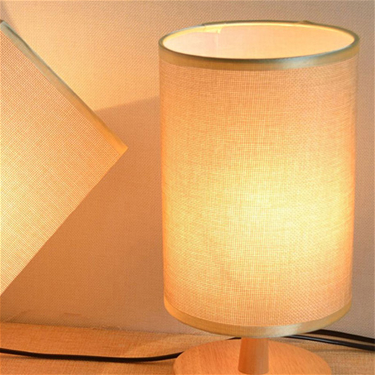 Eine beleuchtete Lampe mit beigem Schirm. Das Licht scheint von der Lampe. Eine zweite Lampe im Hintergrund.