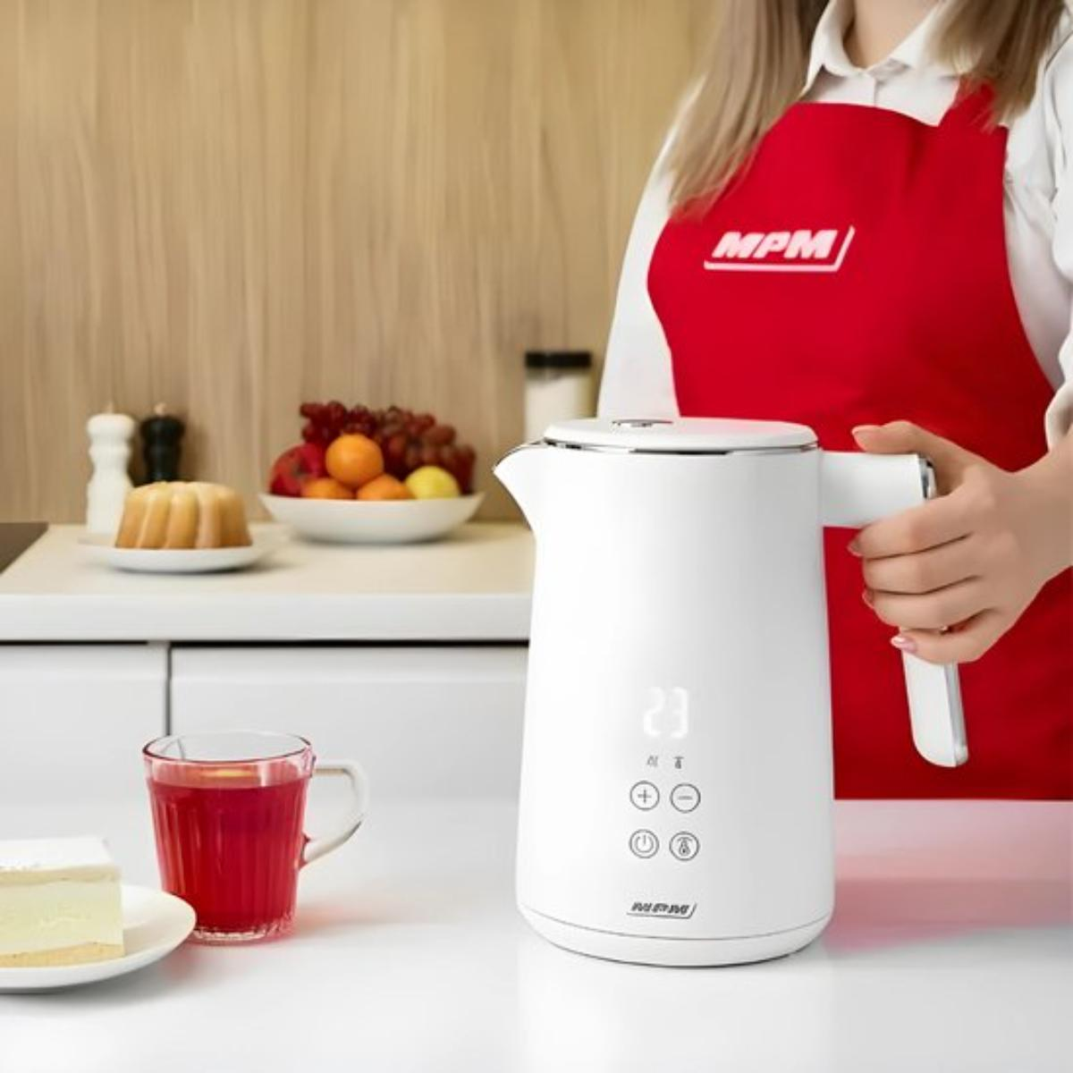 Eine Frau in roter Schürze mit einem weißen Wasserkocher und Tischgedeck.