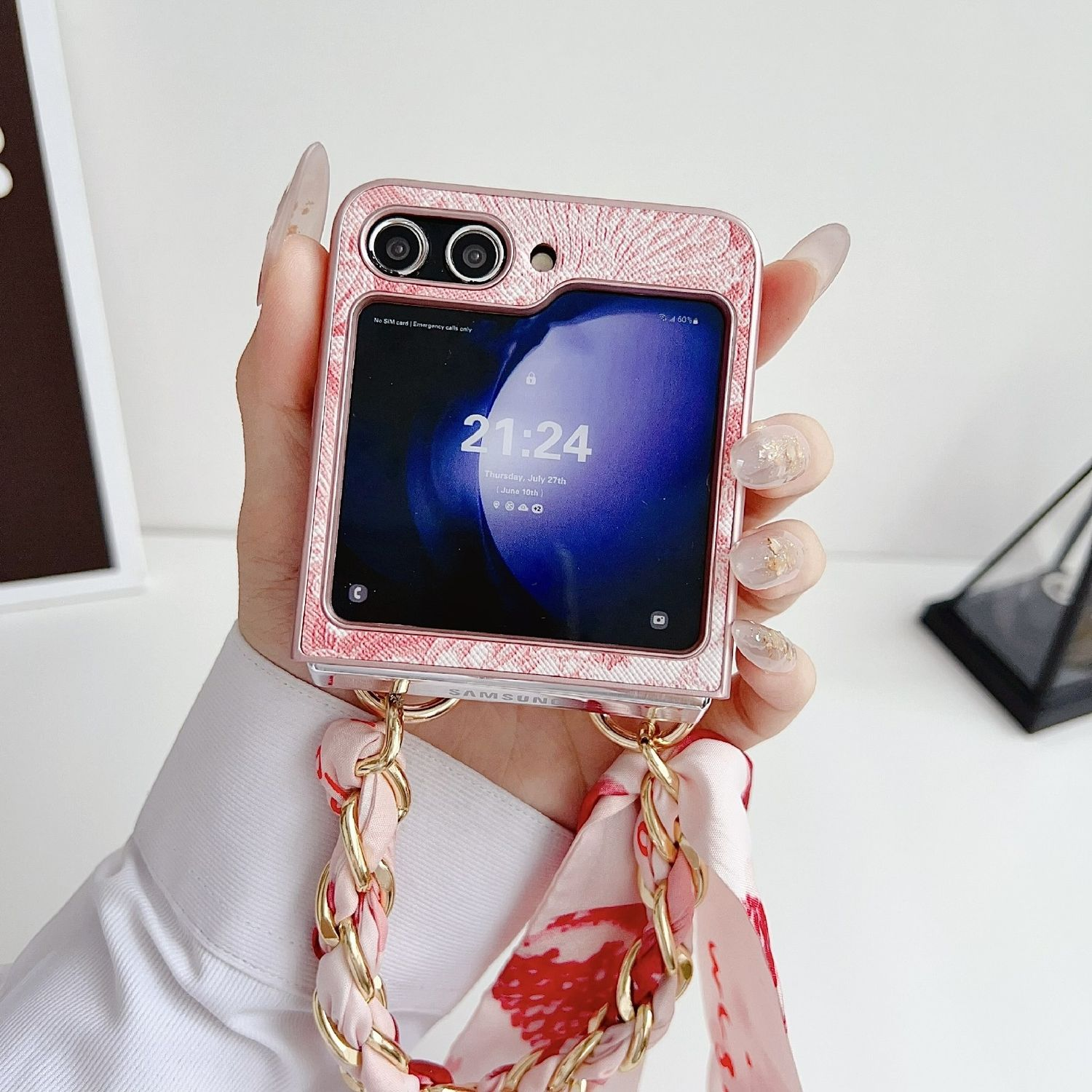 Mano sosteniendo una funda rosa para teléfono con un teléfono Samsung. Hay una correa rosa tipo bufanda.
