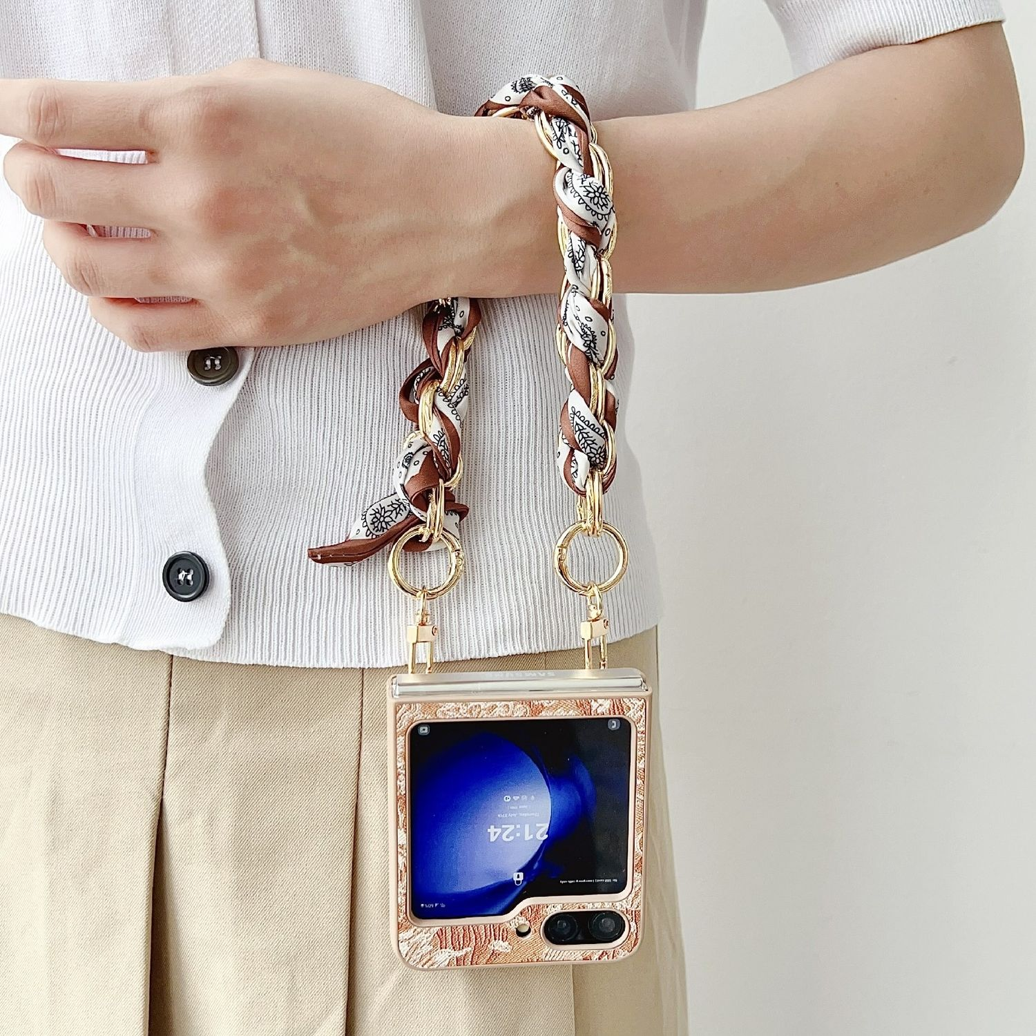La mano de una mujer sosteniendo una cadena dorada y marrón con una funda de teléfono adjunta. El teléfono está abierto.