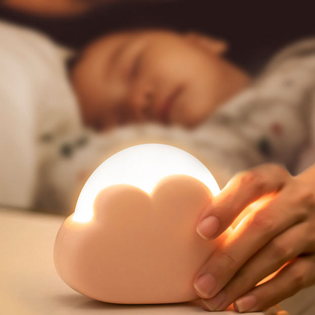 Ein schlafendes Kind, ein wolkenförmiges Nachtlicht und eine Hand, die das Licht berührt.