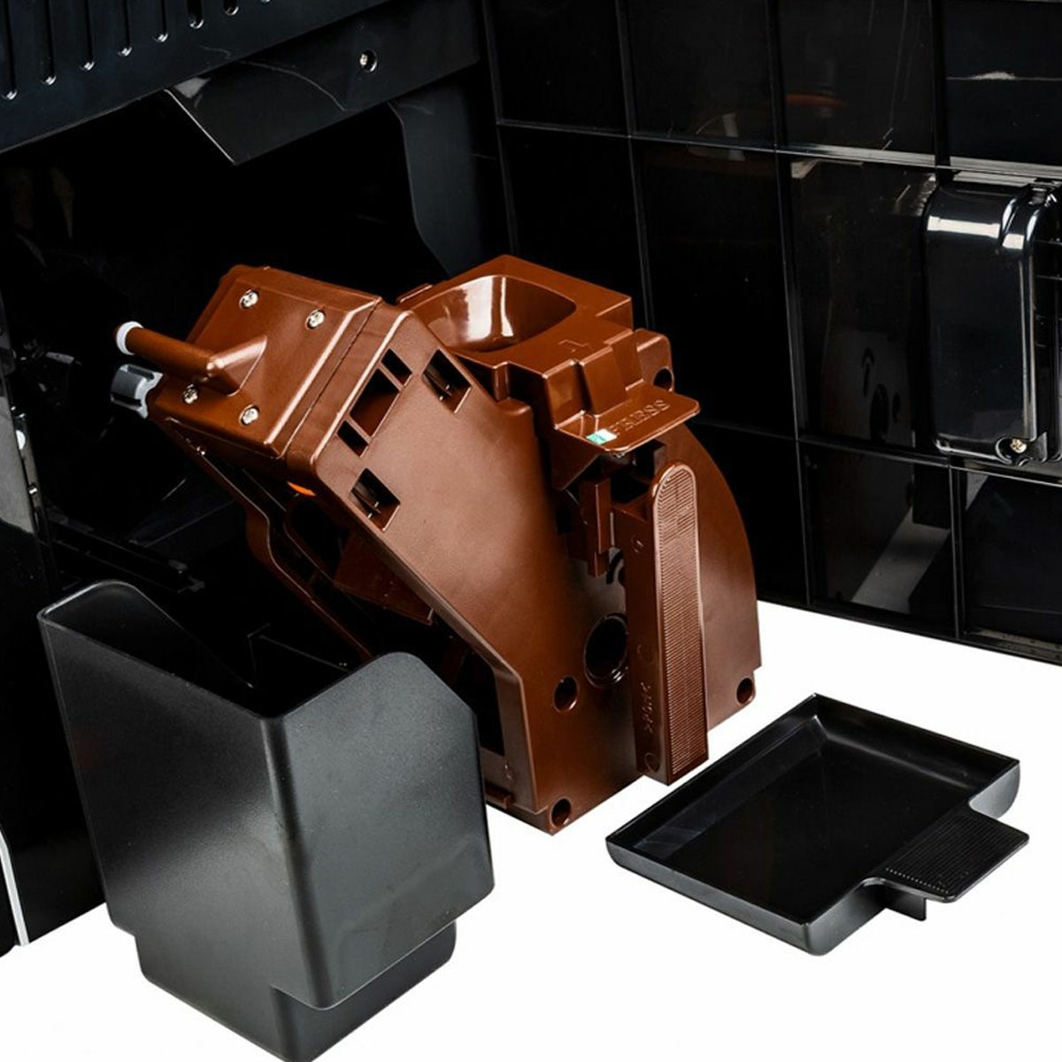 Zdemontowane części ekspresu do kawy: brązowy blok zaparzający, czarny pojemnik na wodę i taca.