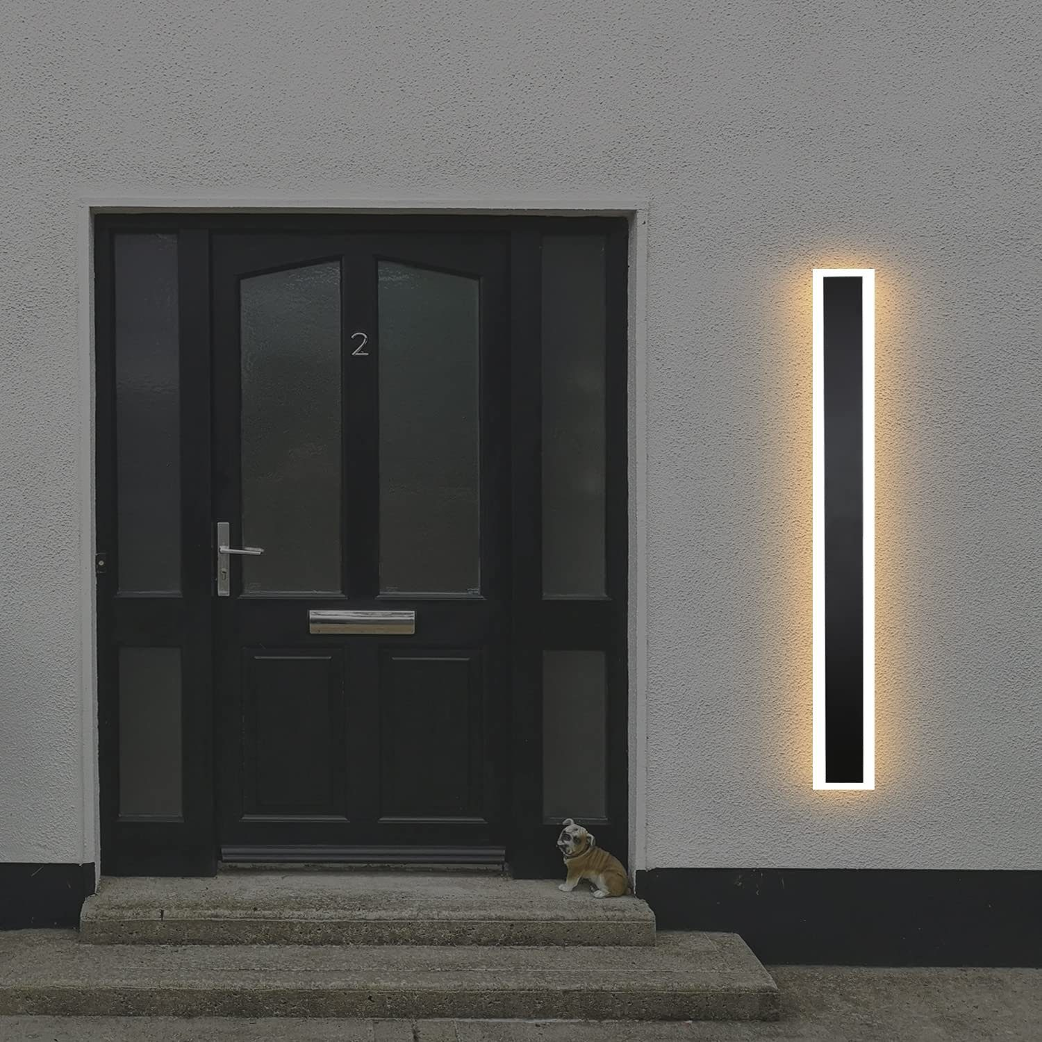 Una porta nera con una luce verticale a destra, una statua di cane sui gradini.
