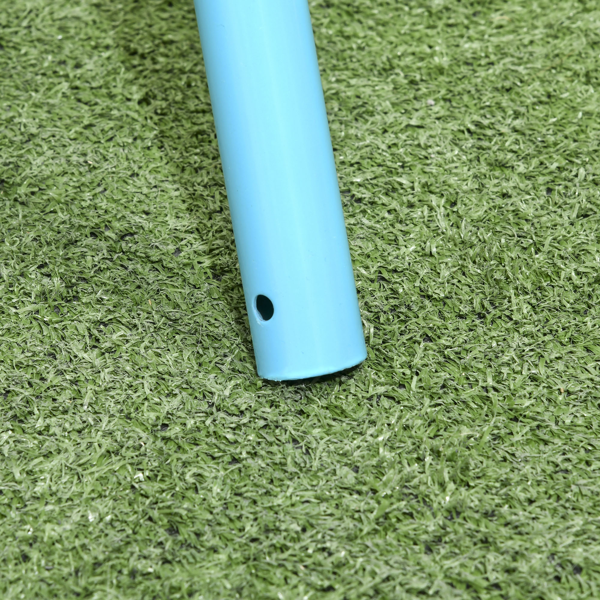 Un primo piano di un palo blu su erba verde, vicino alla sua base con un foro nero.