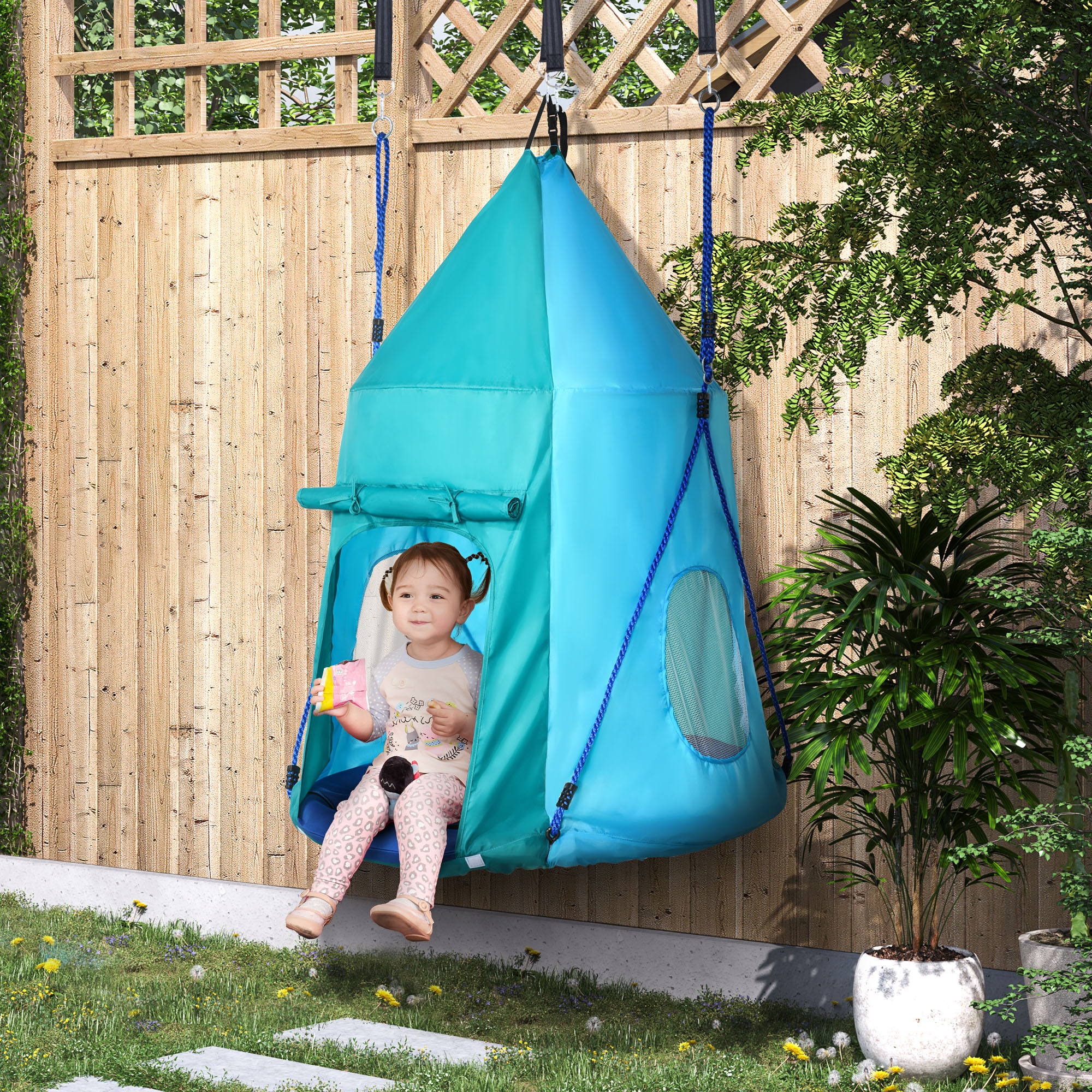 Una bambina è seduta in una tenda altalena verde acqua e blu appesa a una staccionata di legno.