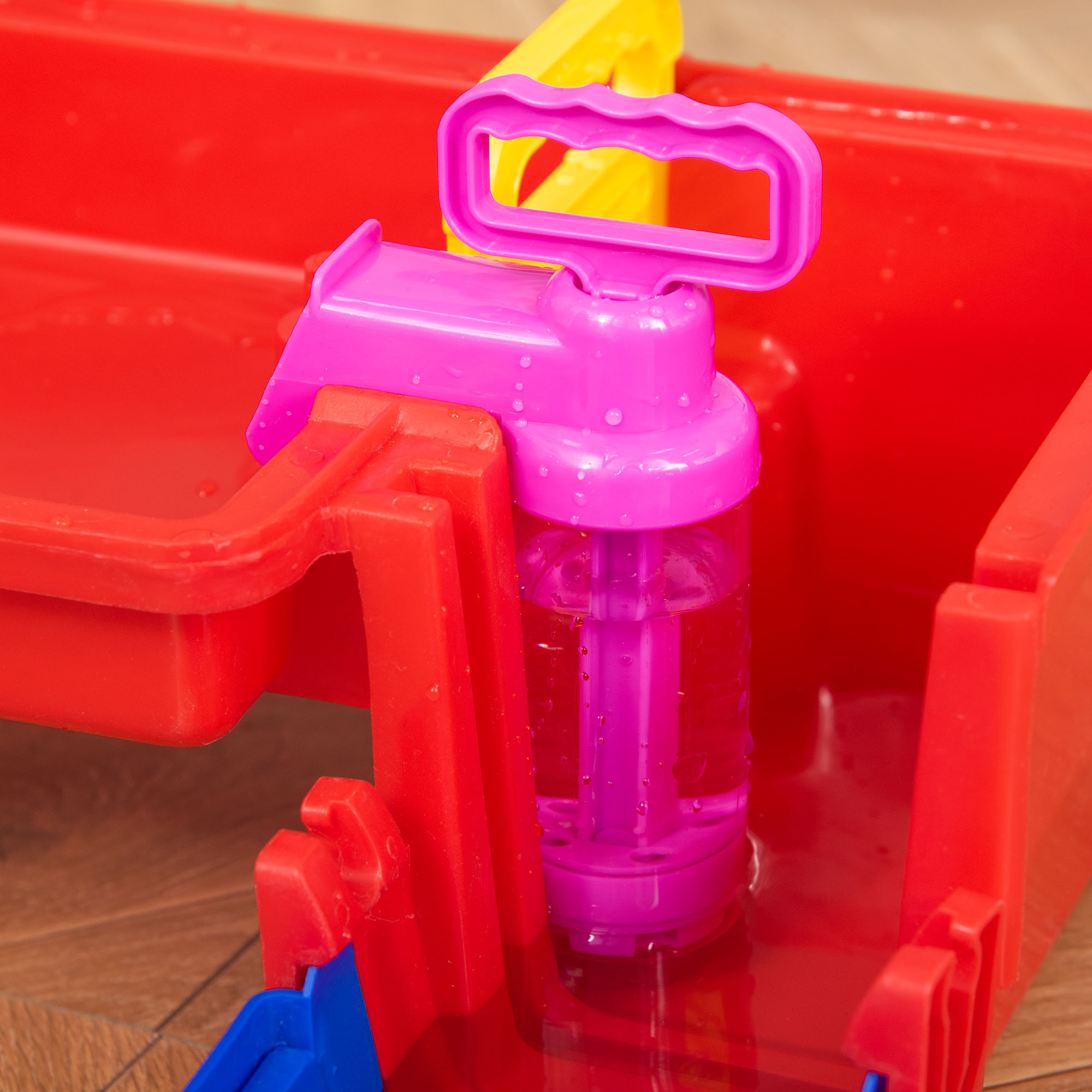 Una pistola ad acqua con un contenitore. Contenitore in plastica rossa e pavimento in legno.