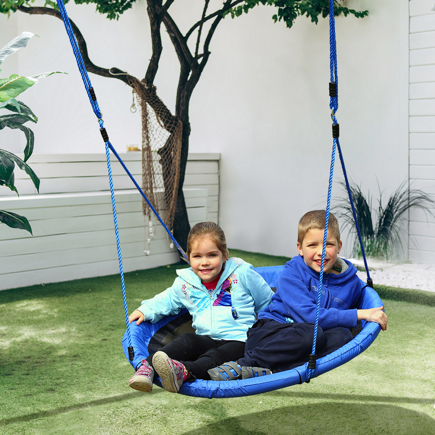 Due bambini sono seduti su un'altalena rotonda blu appesa a un albero. Stanno sorridendo alla fotocamera.