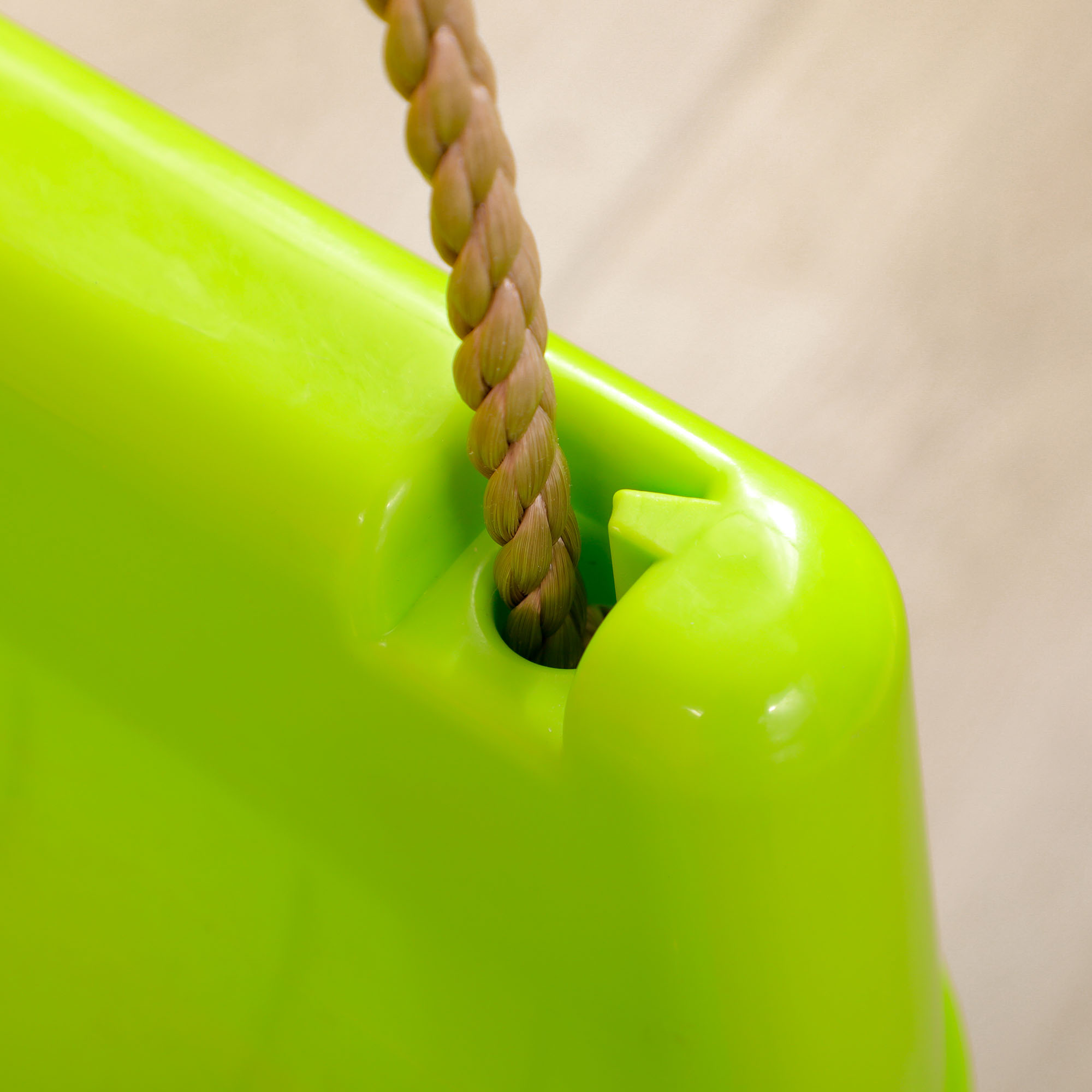 Primo piano di un seggiolino altalena in plastica verde con una corda marrone attaccata. Il sedile è lucido e liscio.