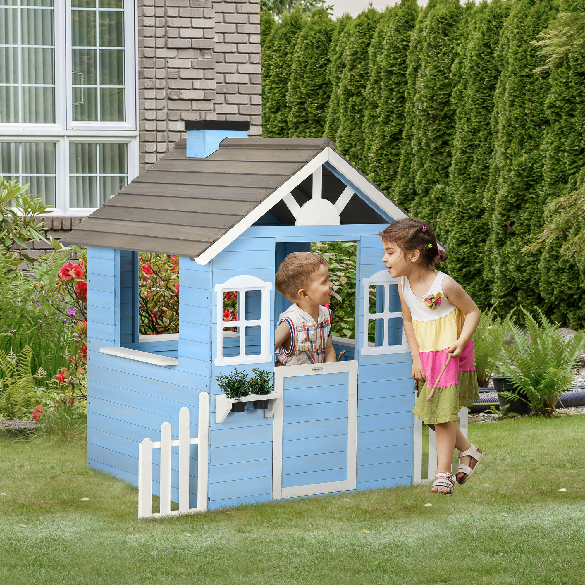 Due bambini giocano in una casetta di legno azzurra con una recinzione bianca in un giardino.