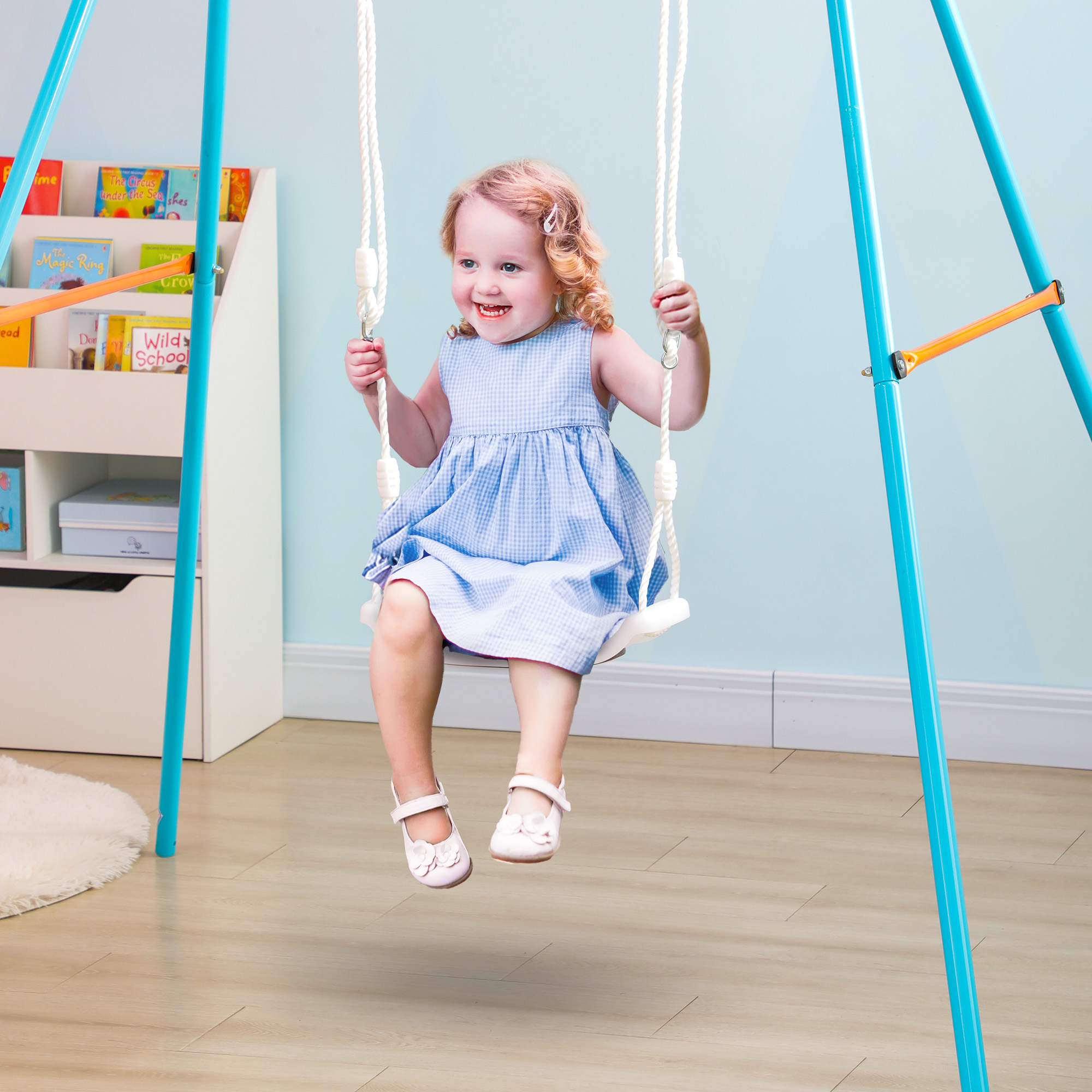Una bambina con un vestito blu si dondola su un'altalena al chiuso. L'altalena è sospesa a un telaio blu.