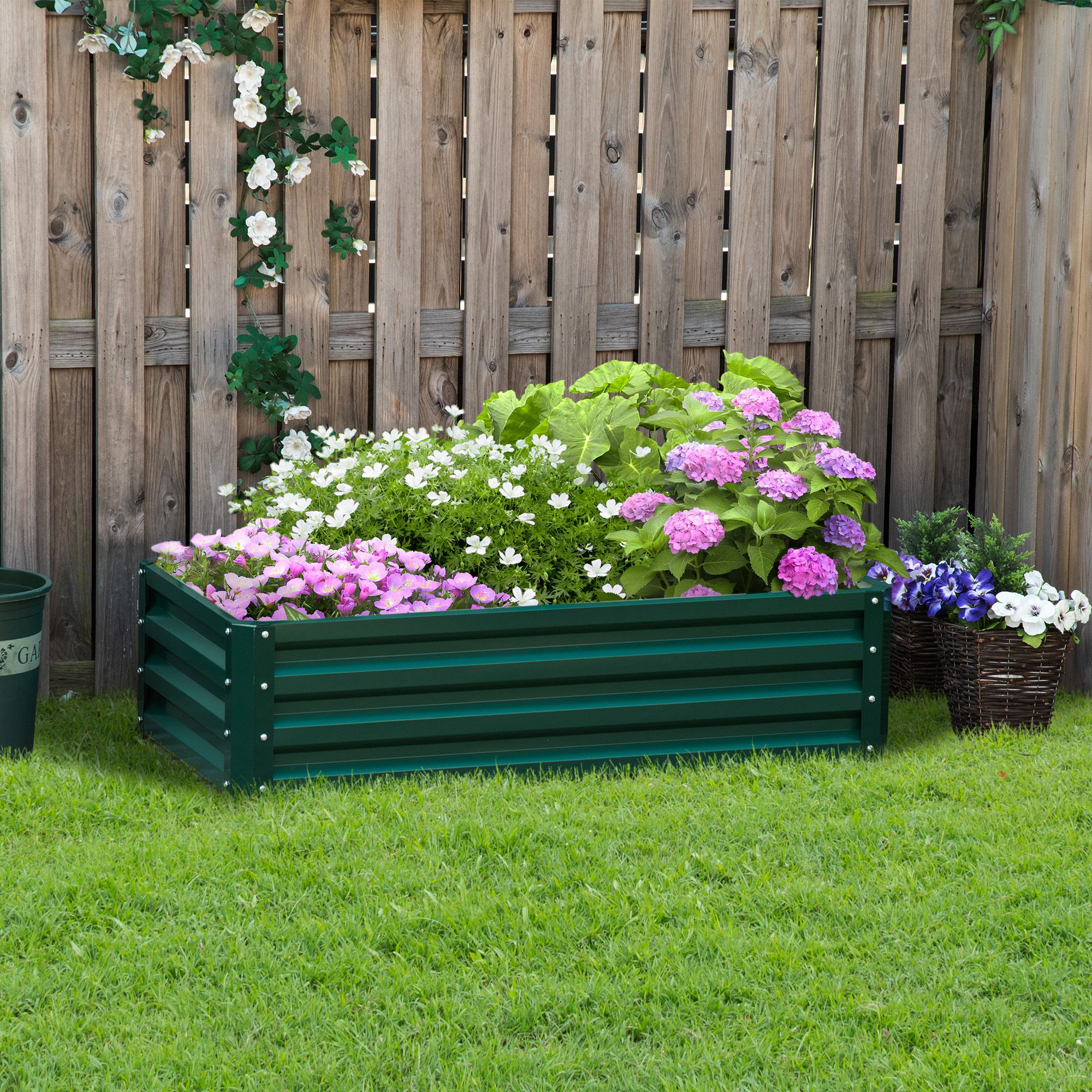 Fioriera in metallo verde sull'erba con fiori e una recinzione in legno sullo sfondo.