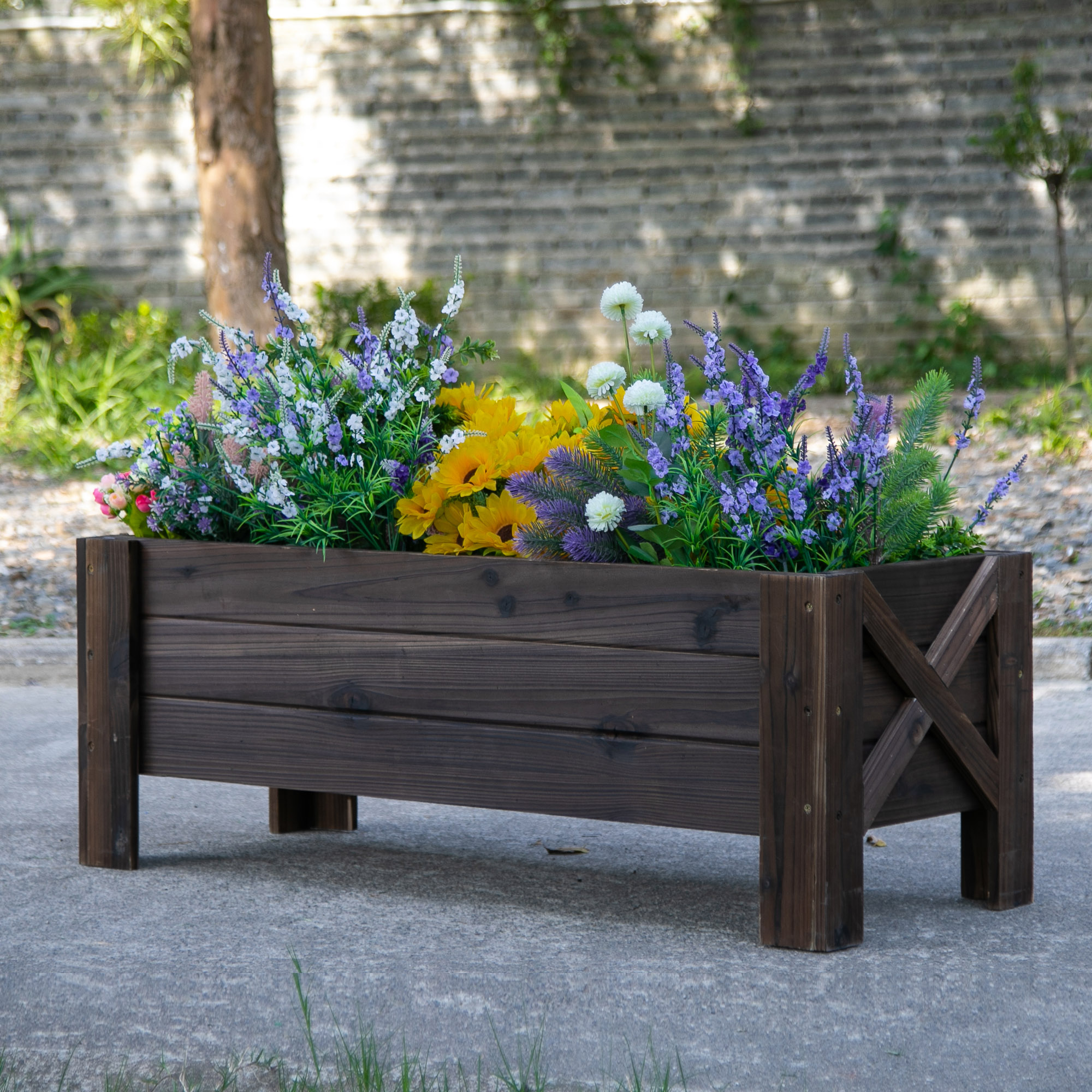 Fioriera in legno con fiori. Sfondo: albero e muro di mattoni.