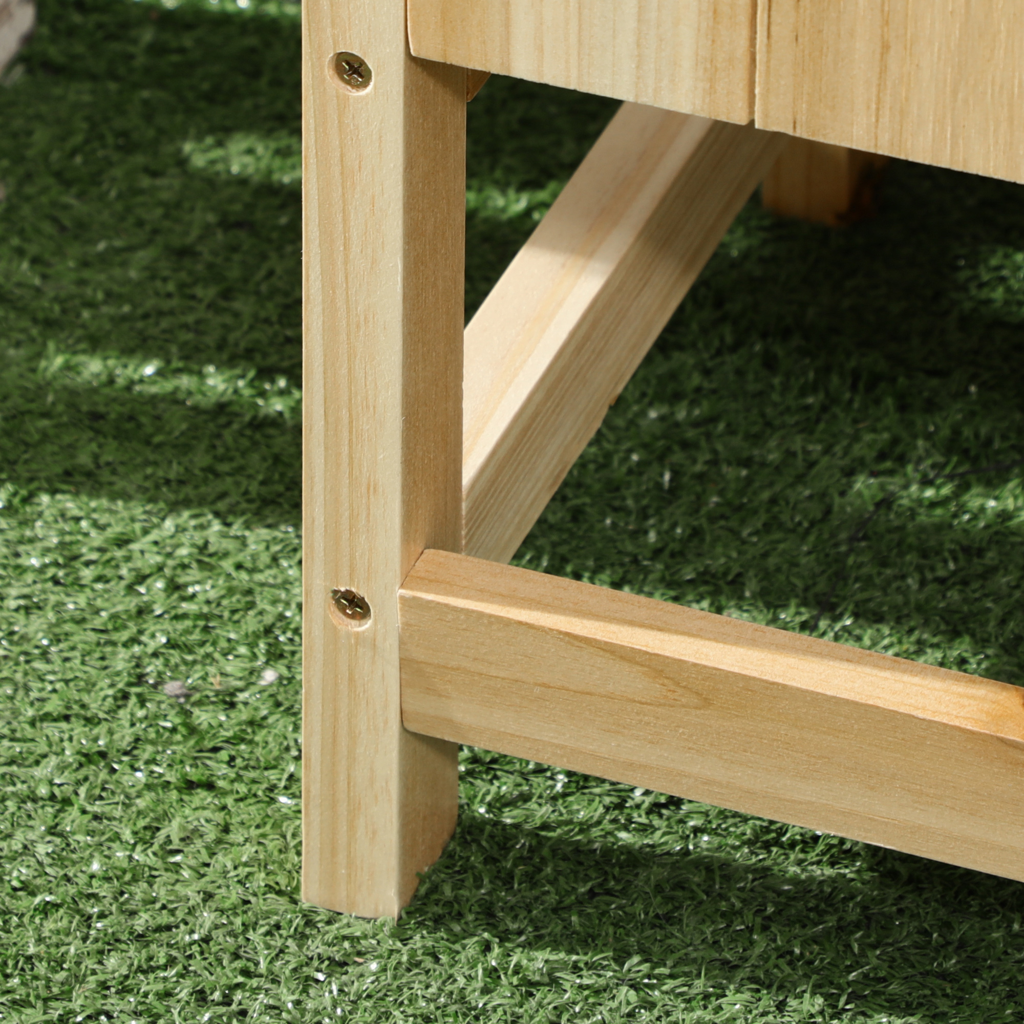 Primo piano della gamba di un tavolo in legno con viti su erba sintetica verde.