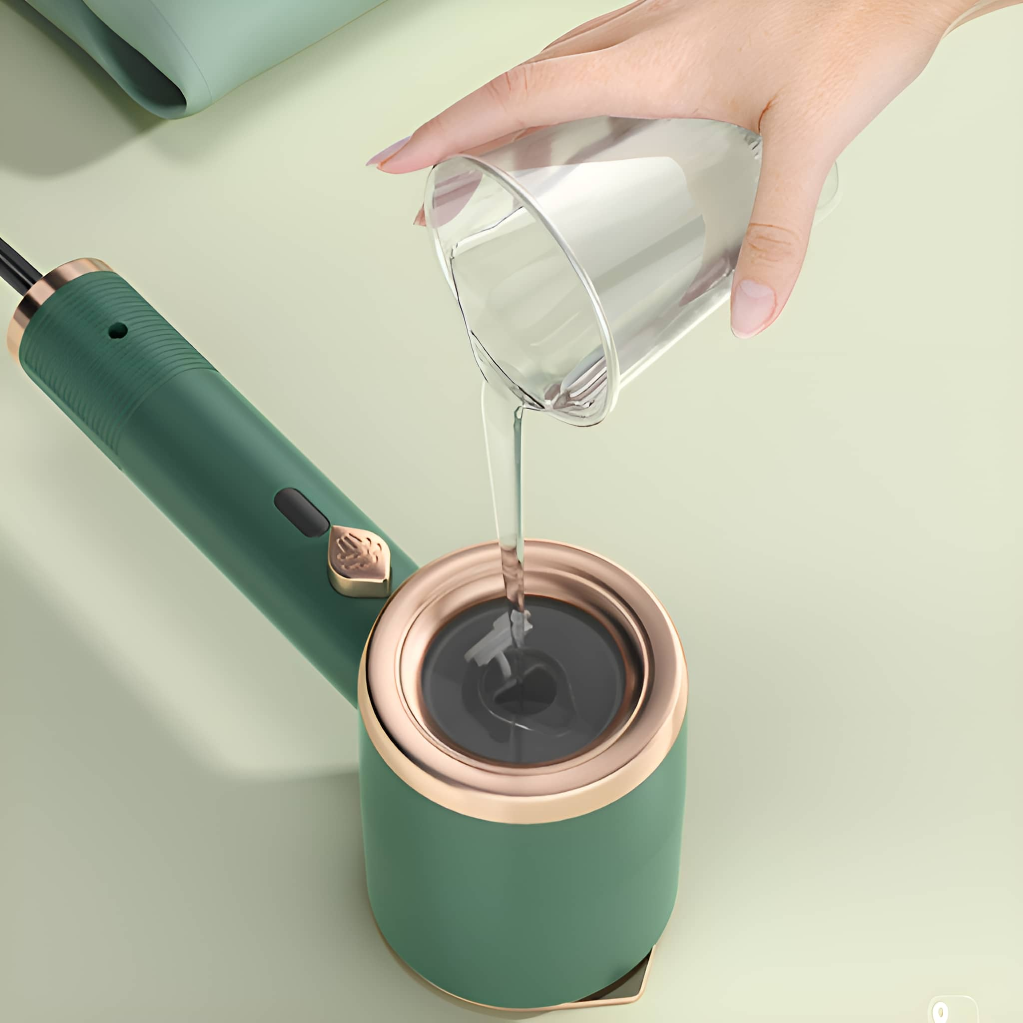 Eine Hand gießt Wasser aus einem Glas in einen grün-goldenen Haardämpfer.