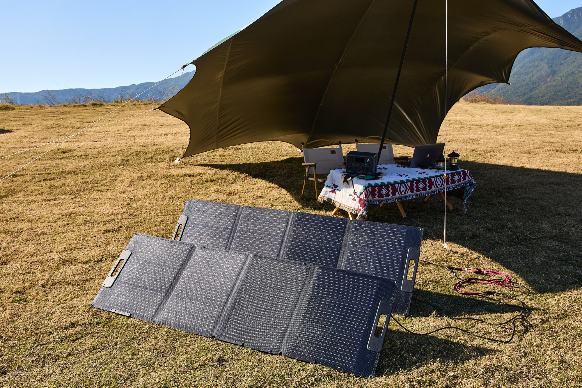 Dwa czarne panele słoneczne na trawie z namiotem i stołem w tle, słoneczny dzień.