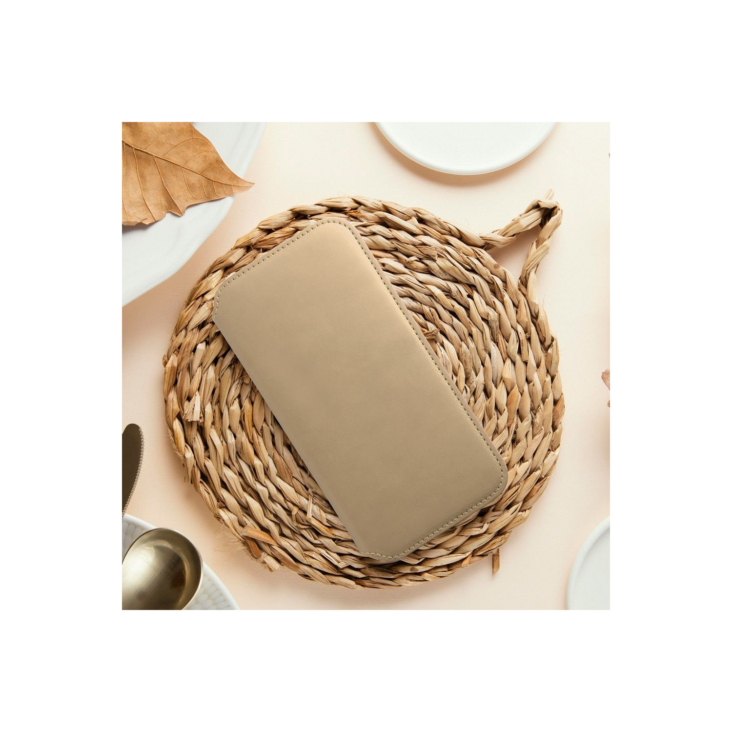 Custodia beige per telefono su tappetino intrecciato con piatti e foglia.