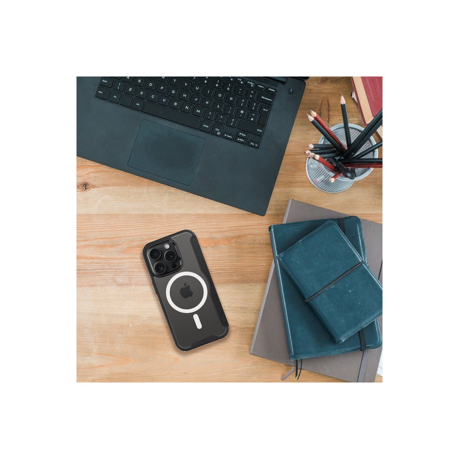 Telefono nero in una custodia trasparente su una superficie di legno. Sono presenti un laptop, quaderni e matite.