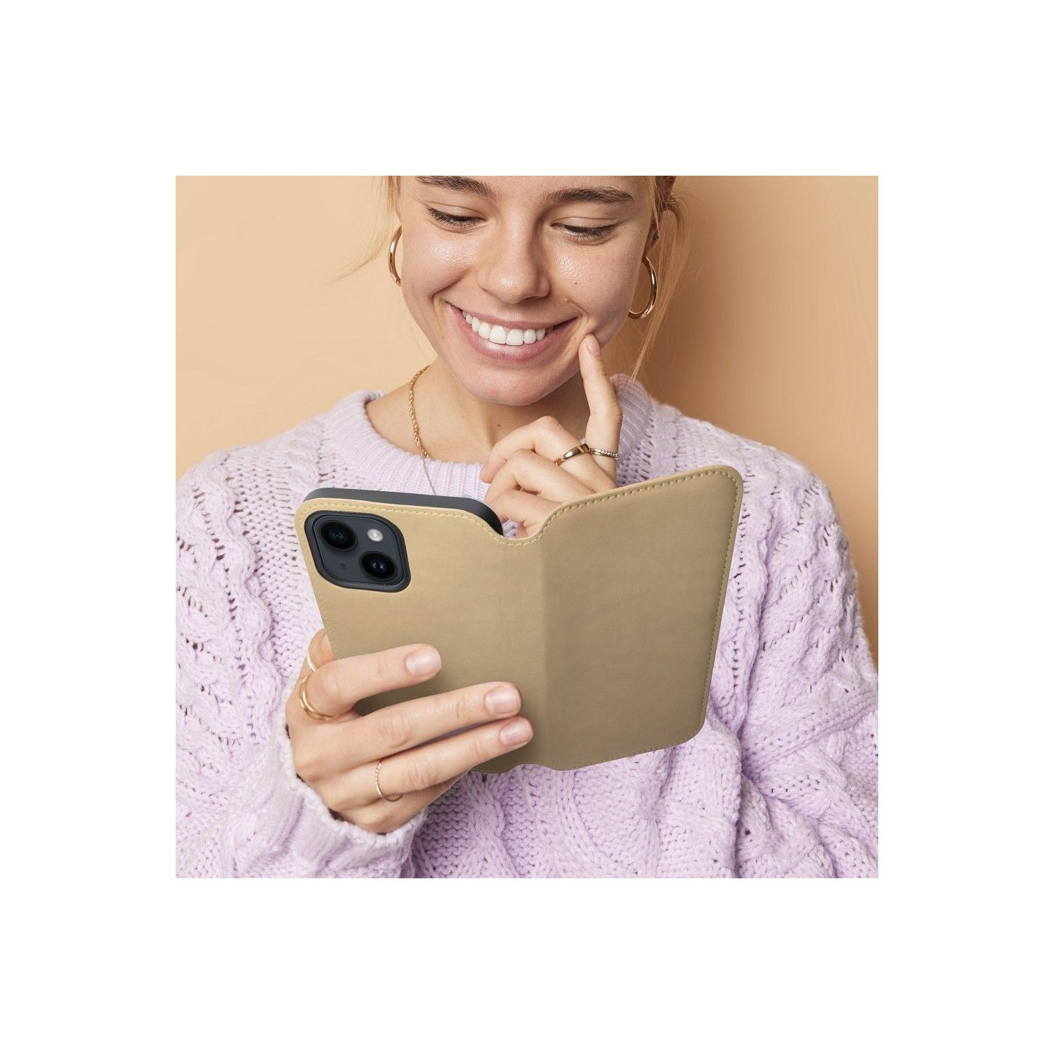 Donna sorride, tiene telefono in custodia beige. Indossa un maglione lilla e gioielli d'oro.