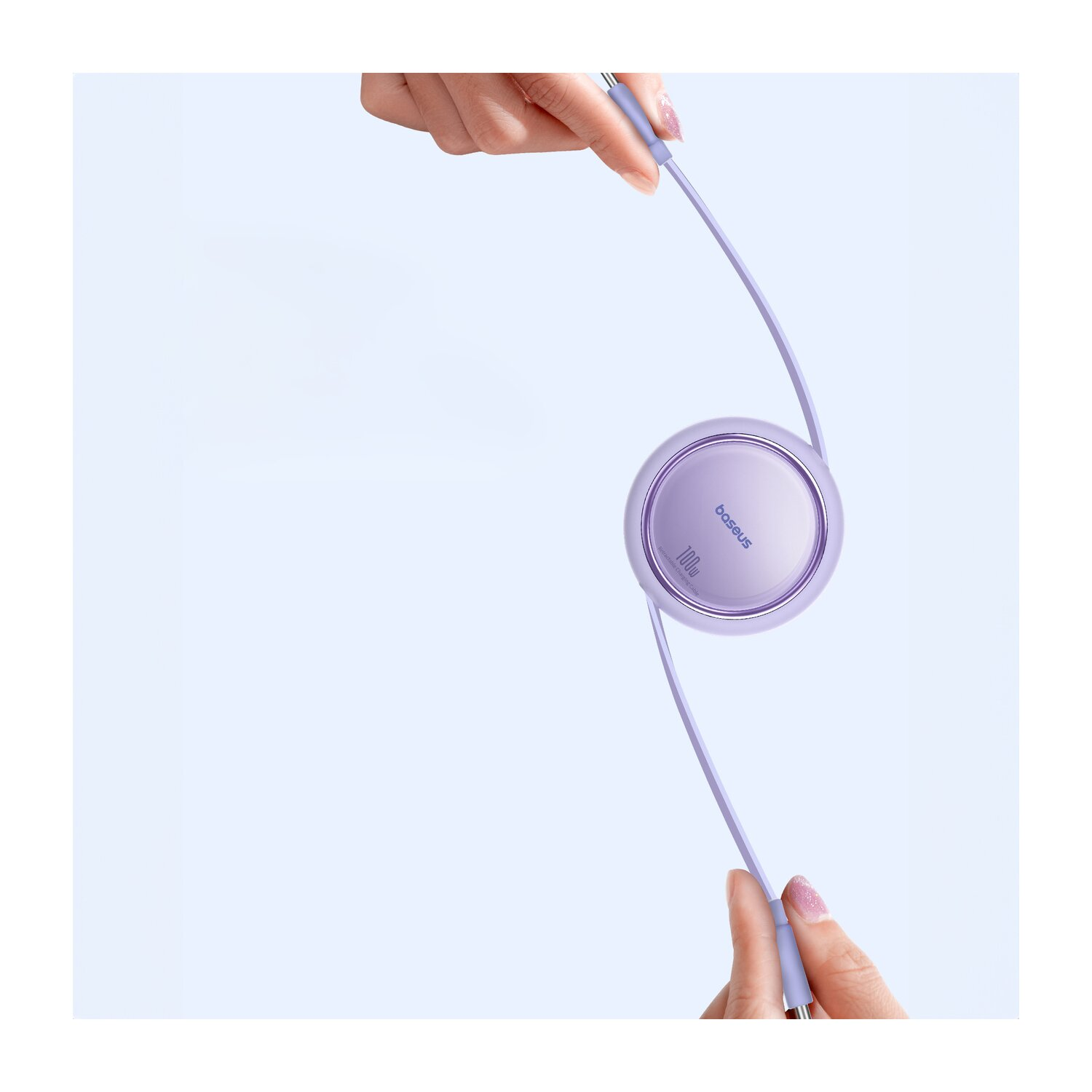 Dwie dłonie trzymają fioletowe okrągłe urządzenie z kablem. Urządzenie posiada logo 'baseus'.