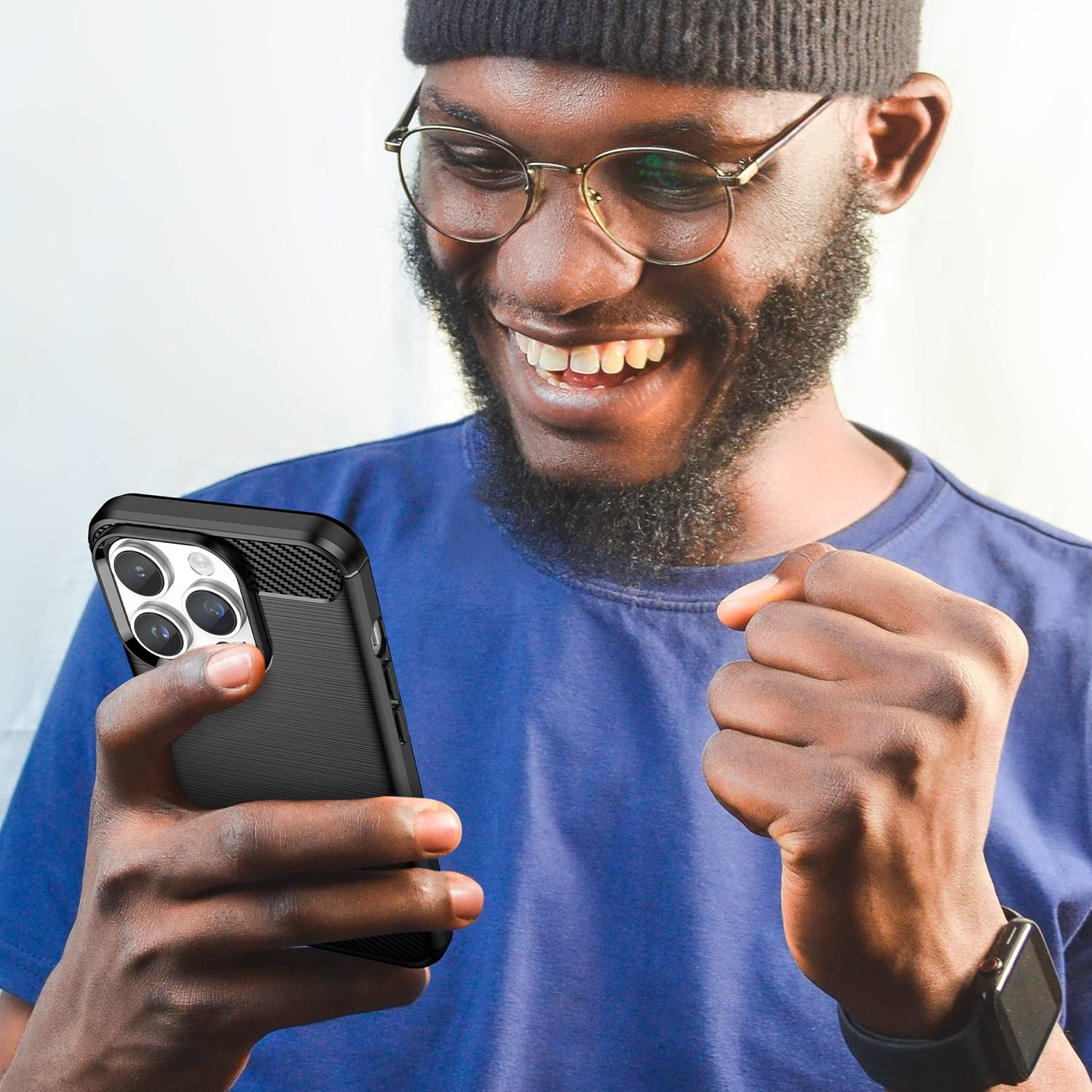 Ein lächelnder Mann hält ein schwarzes Telefon mit Hülle. Er trägt eine Brille, ein blaues Hemd und eine Uhr.