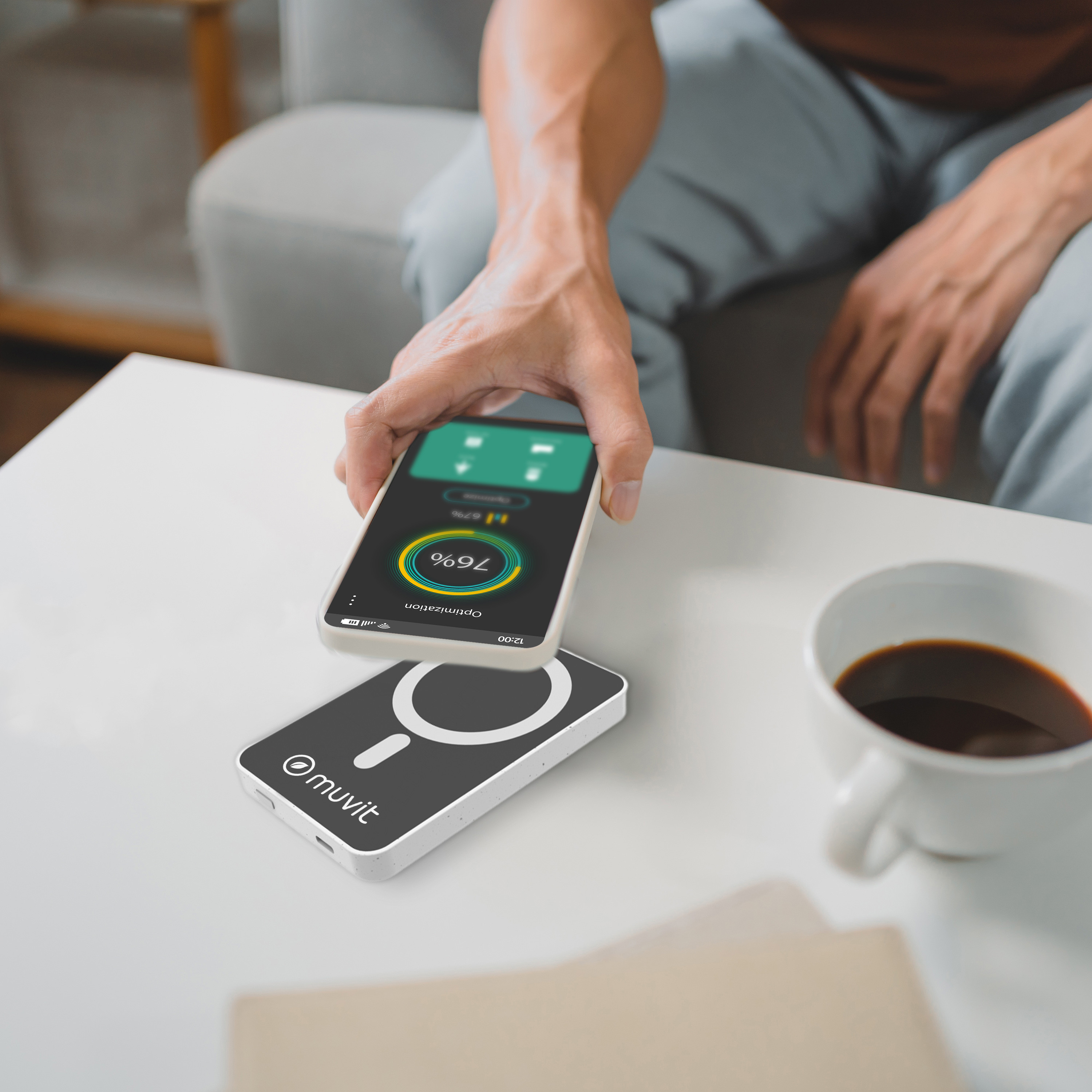 Una persona cargando un teléfono de forma inalámbrica. Un cargador y una taza de café en la mesa. Fondo blanco.