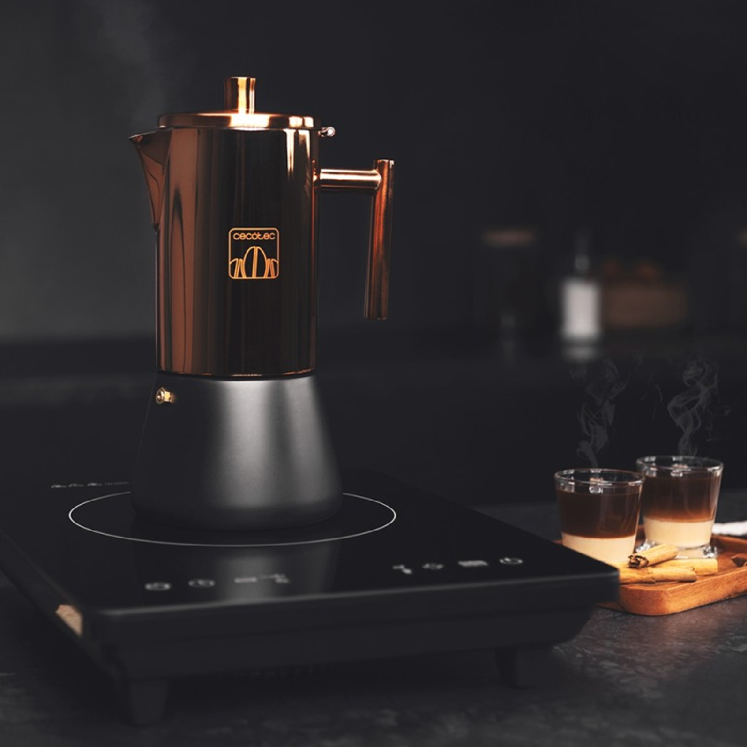 Ekspres do kawy z dwoma szklankami kawy i laskami cynamonu na czarnej powierzchni.