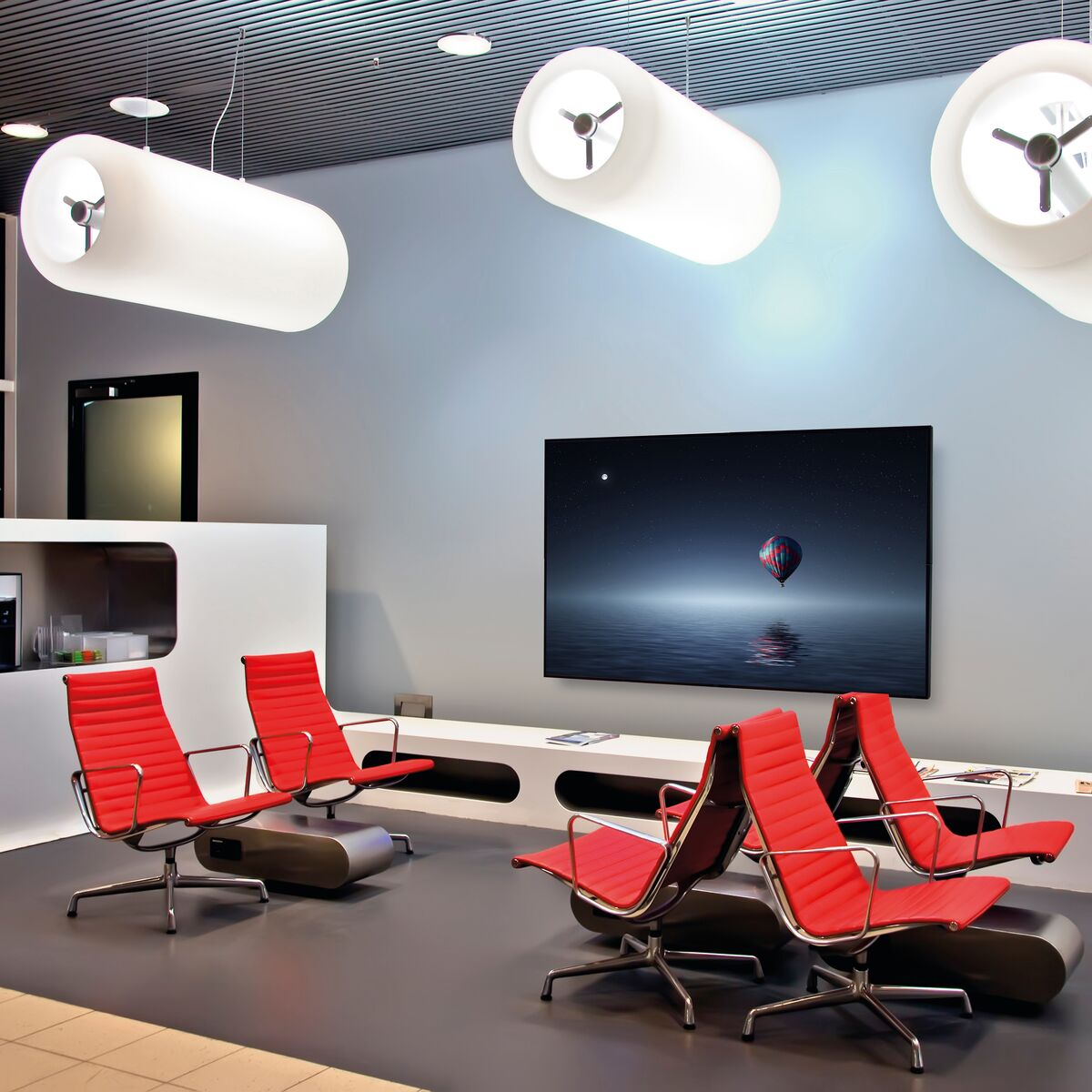 Modern waiting area with red chairs, a large screen and artistic lighting.