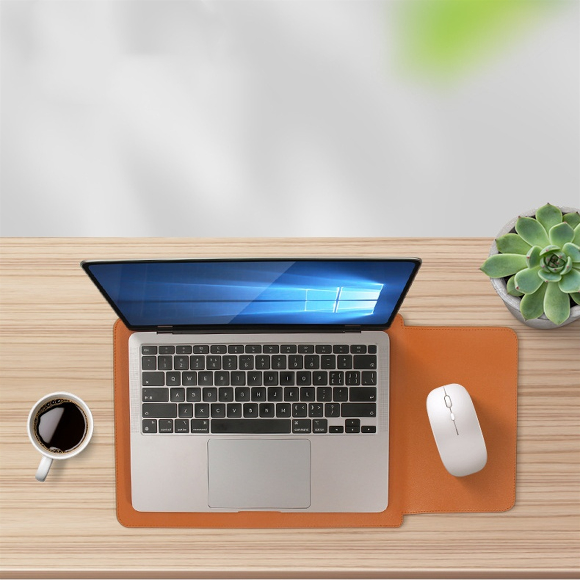 Laptop, Kaffeetasse und Maus auf einem Holzschreibtisch, Pflanze im Hintergrund.