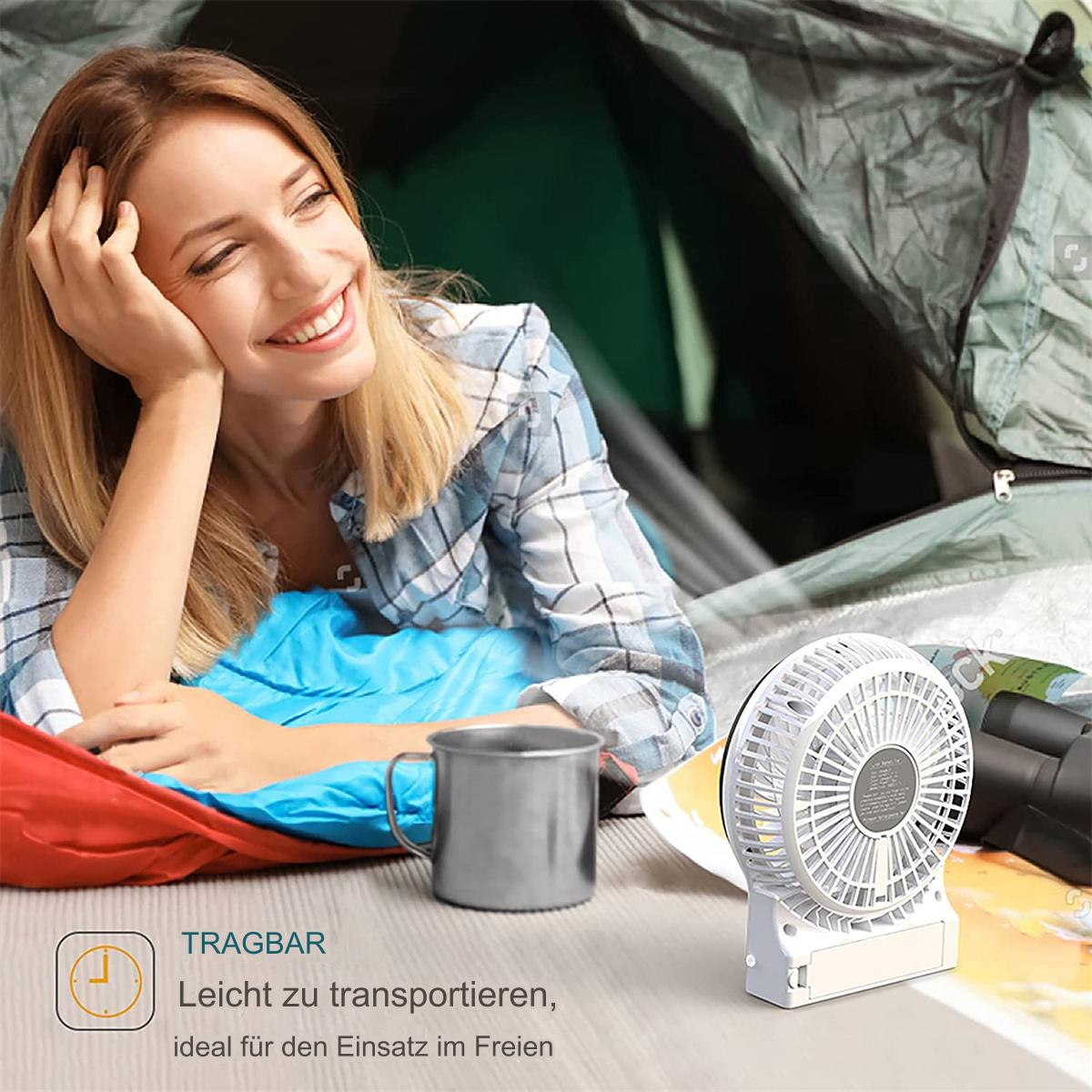 Frau lächelt in einem Zelt, mit einem Ventilator, einem Becher und anderen Campingartikeln.