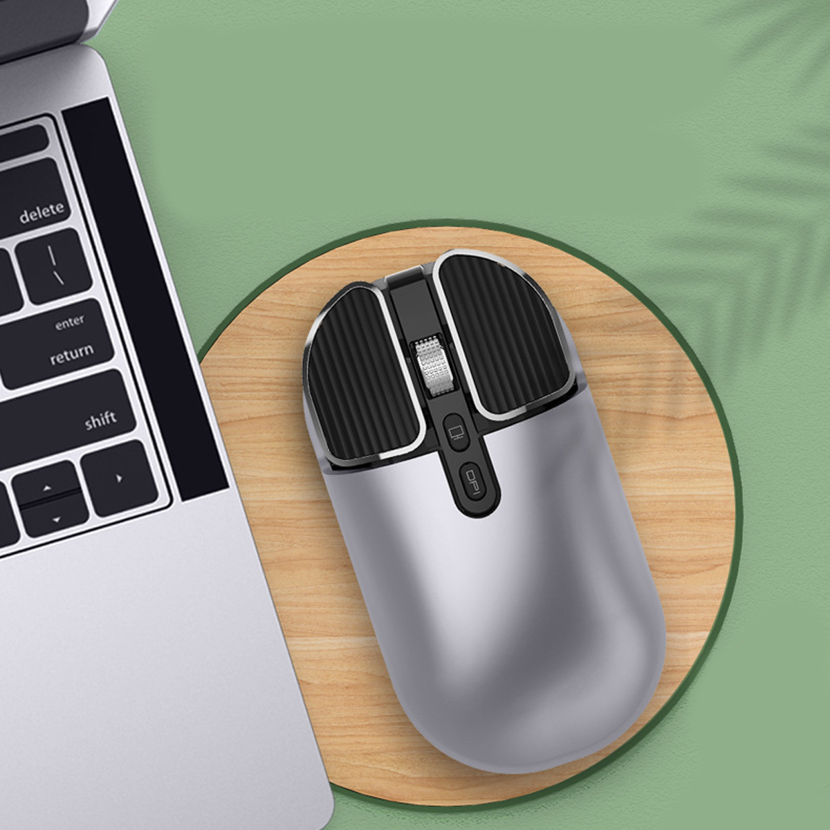 Silberfarbene kabellose Maus mit schwarzen Akzenten, auf Holzuntersetzer, neben Laptop.