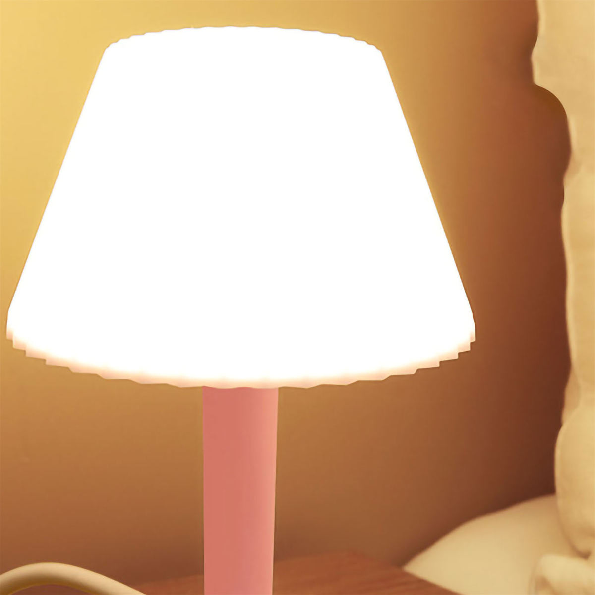 Eine beleuchtete rosa Lampe mit weißem Lampenschirm. Der Hintergrund ist eine beige Wand.