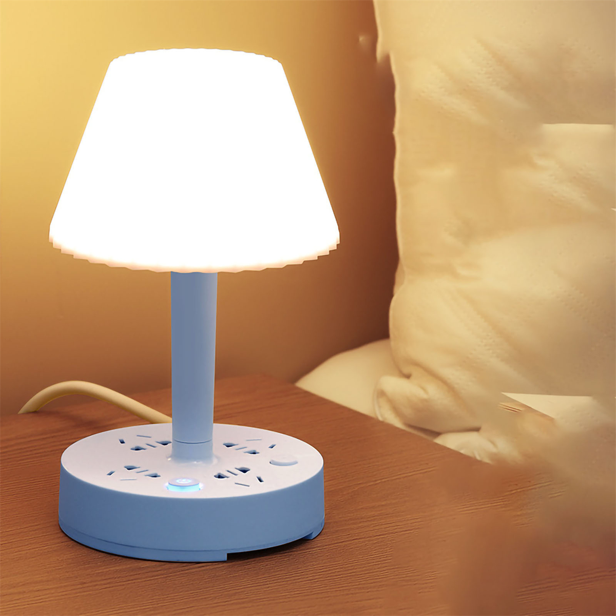 Eine weiße Lampe mit blauem Sockel auf einem braunen Tisch. Sie hat einen weißen Lampenschirm und Steckdosen.