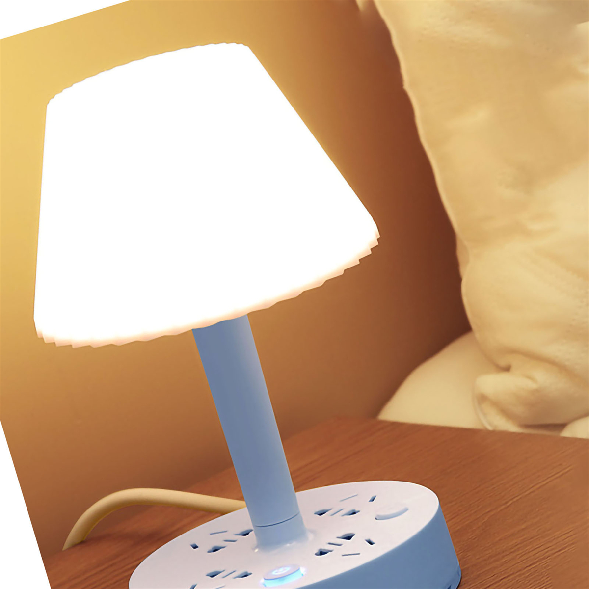 Lampe auf einem Tisch mit mehreren Steckdosen. Die Lampe hat einen weißen Schirm und einen blauen Sockel.