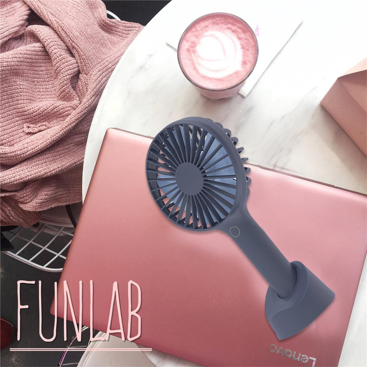 Ein Handventilator auf einem rosa Laptop, mit einer Kaffeetasse und einem rosa Pullover.