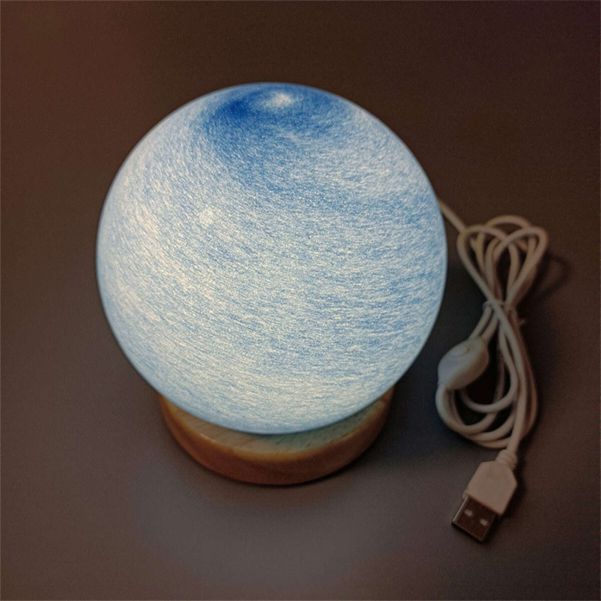 Mondförmige Lampe auf Holzsockel, mit USB-Kabel und Knopf. Blaue Oberfläche.