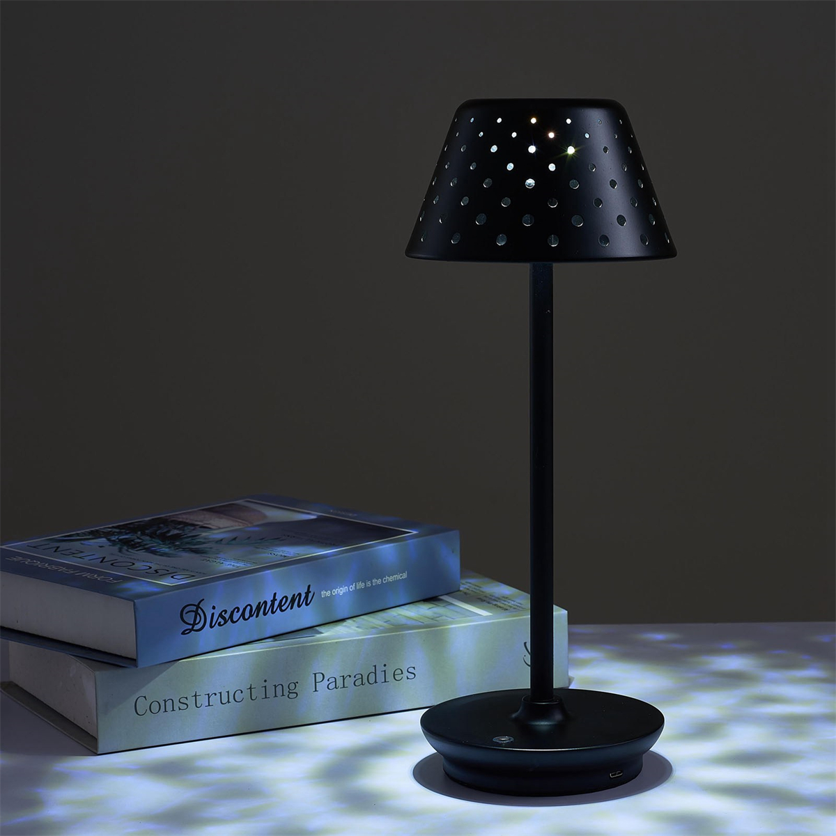 Eine schwarze Tischlampe mit perforiertem Schirm, Büchern und dunklem Hintergrund.