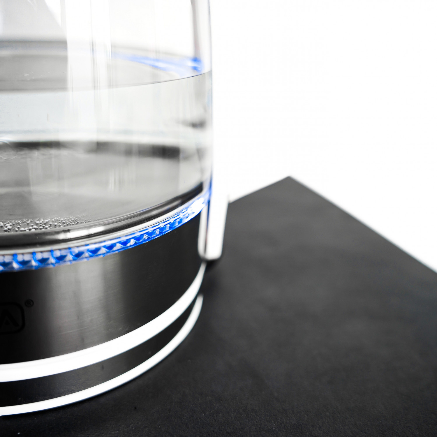 Elektrischer Glaskessel mit Wasser, auf schwarzer Oberfläche und weißem Hintergrund.