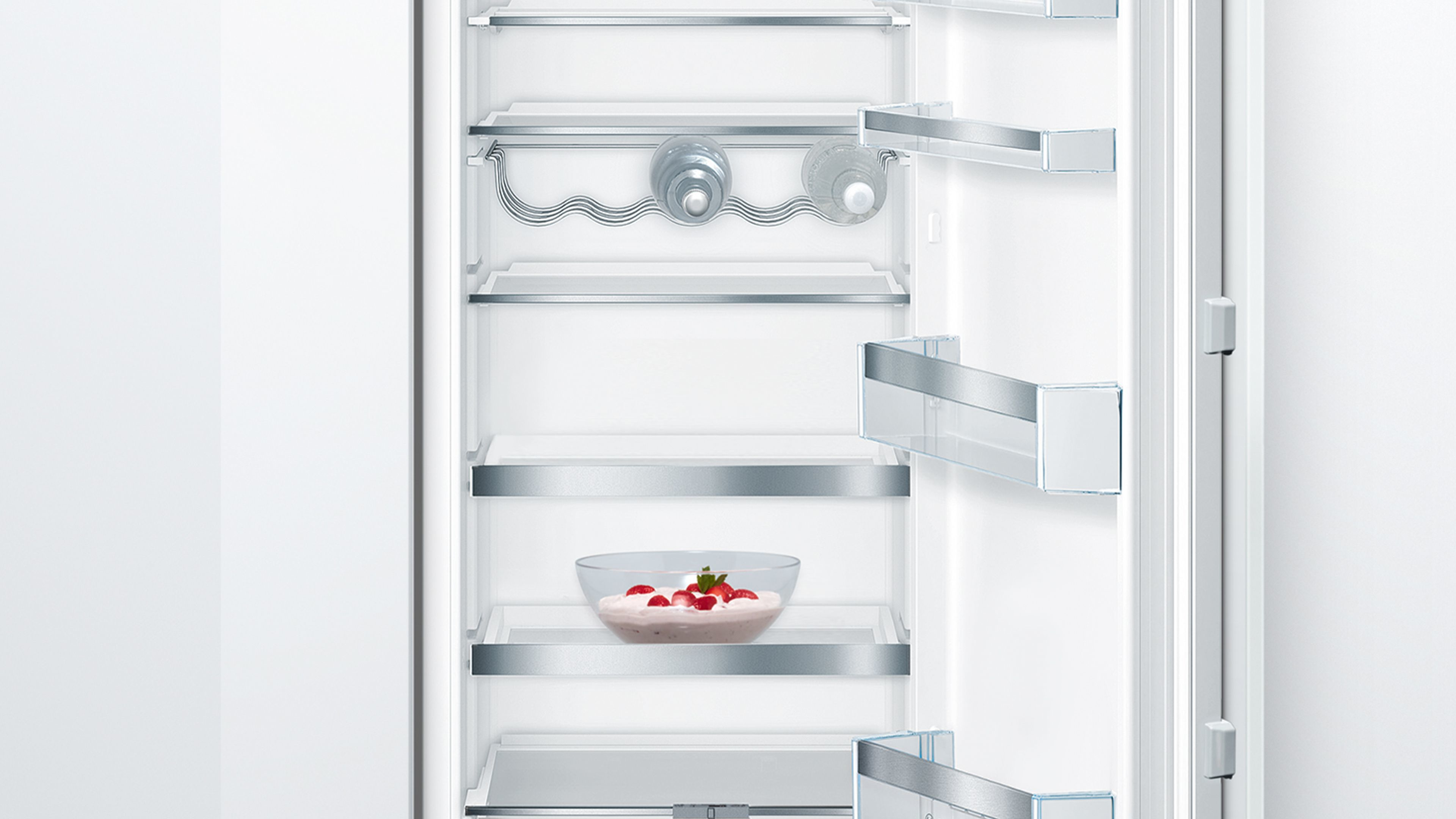 Inside a white refrigerator with shelves, bottles, and a bowl of strawberries.