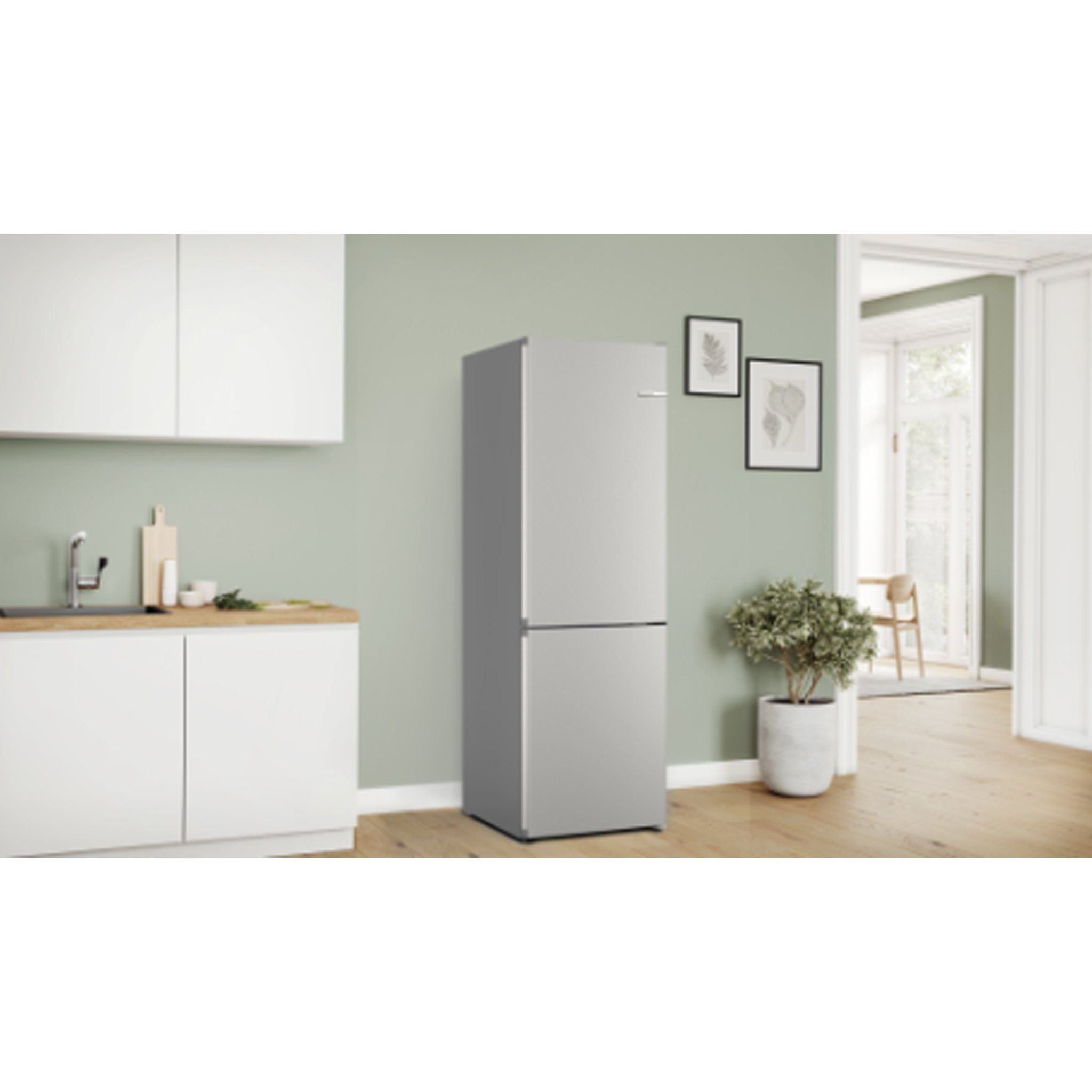 Un refrigerador plateado en una cocina junto a gabinetes blancos y una planta. La puerta está cerrada.