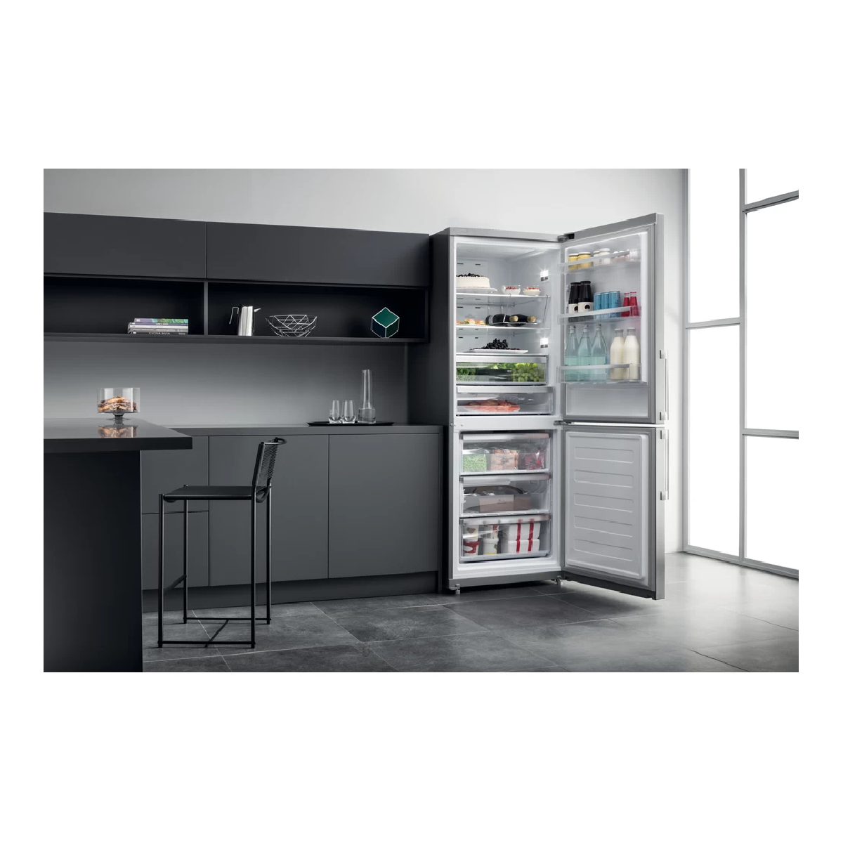 Cucina moderna con frigorifero con porte aperte. C'è un bancone nero con uno sgabello.