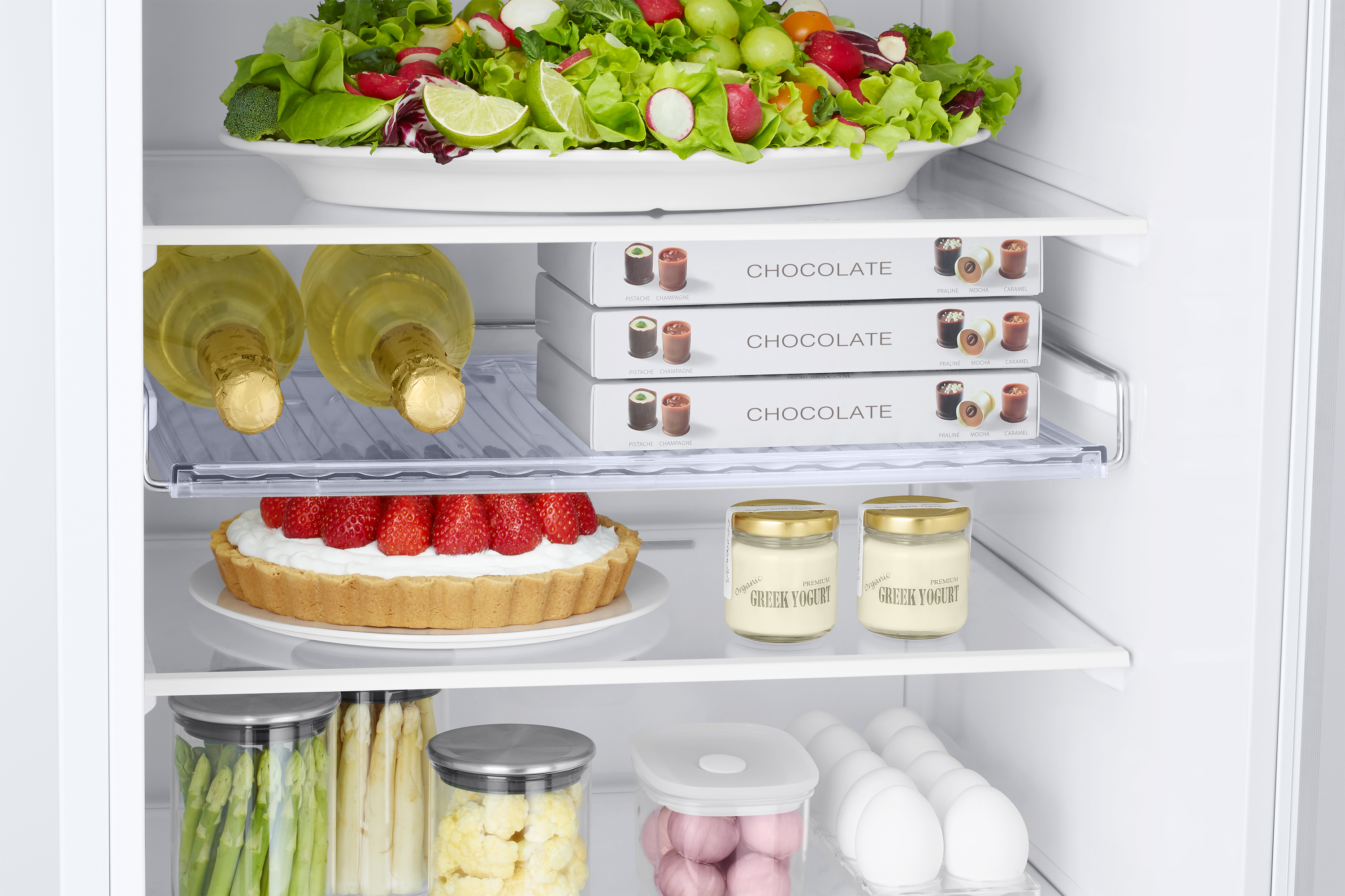 Refrigerator interior with food: salad, strawberries, yogurt, and chocolates.
