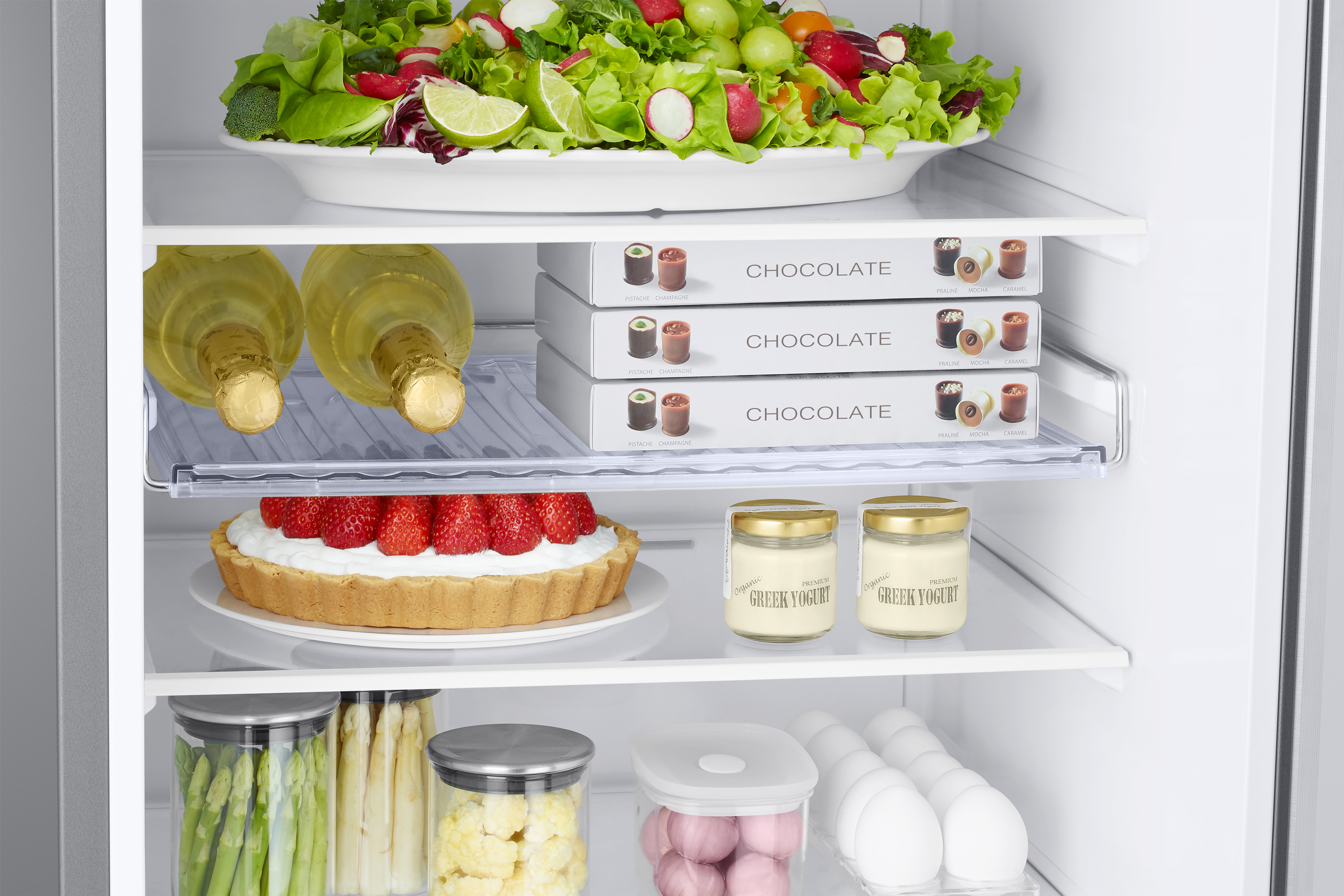 Interior de un frigorífico con alimentos, incluyendo ensalada, cajas de chocolate, yogur y fresas.